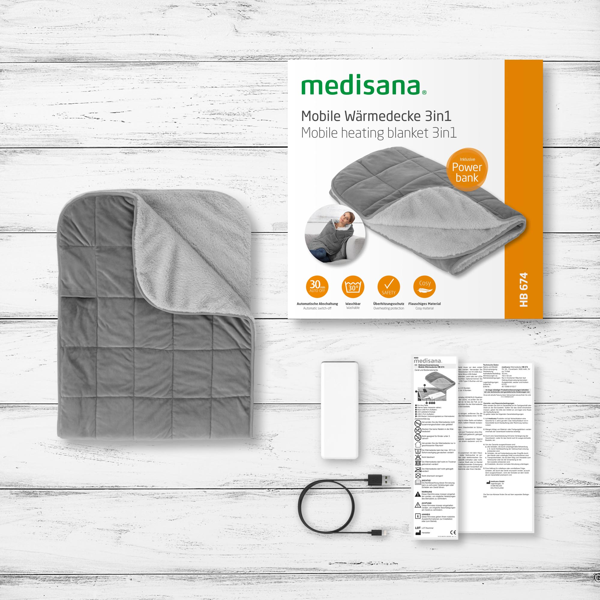 Una coperta riscaldata grigia con controllo bianco. La scatola mostra la coperta e gli accessori su un tavolo di legno.