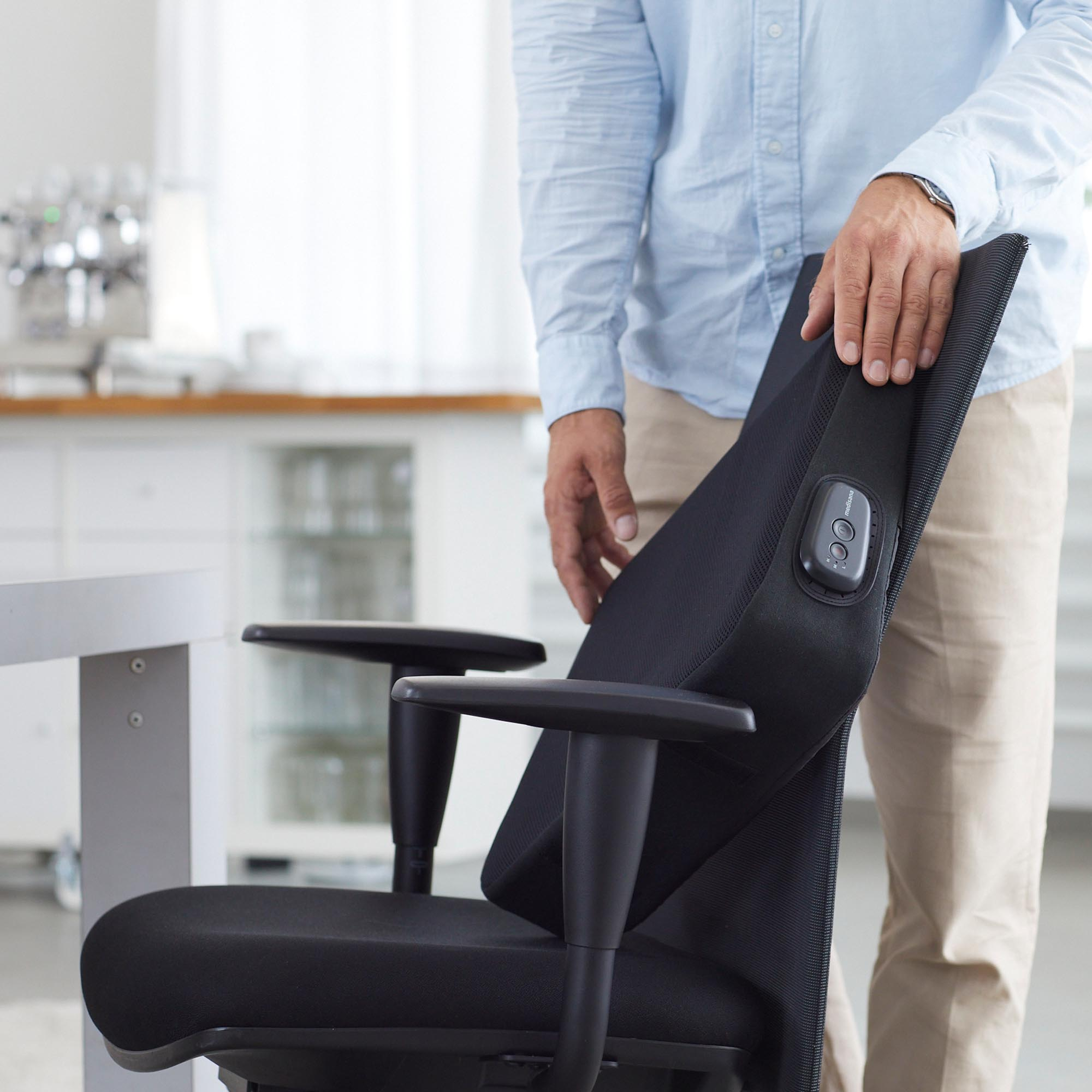 A person's hand on the back of a black office chair in a room.
