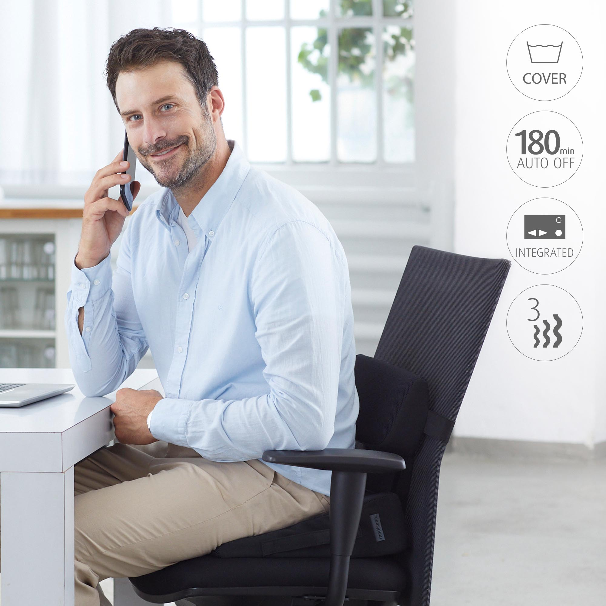 Man in blue shirt, using phone, sitting at a white desk. Black chair with back support.