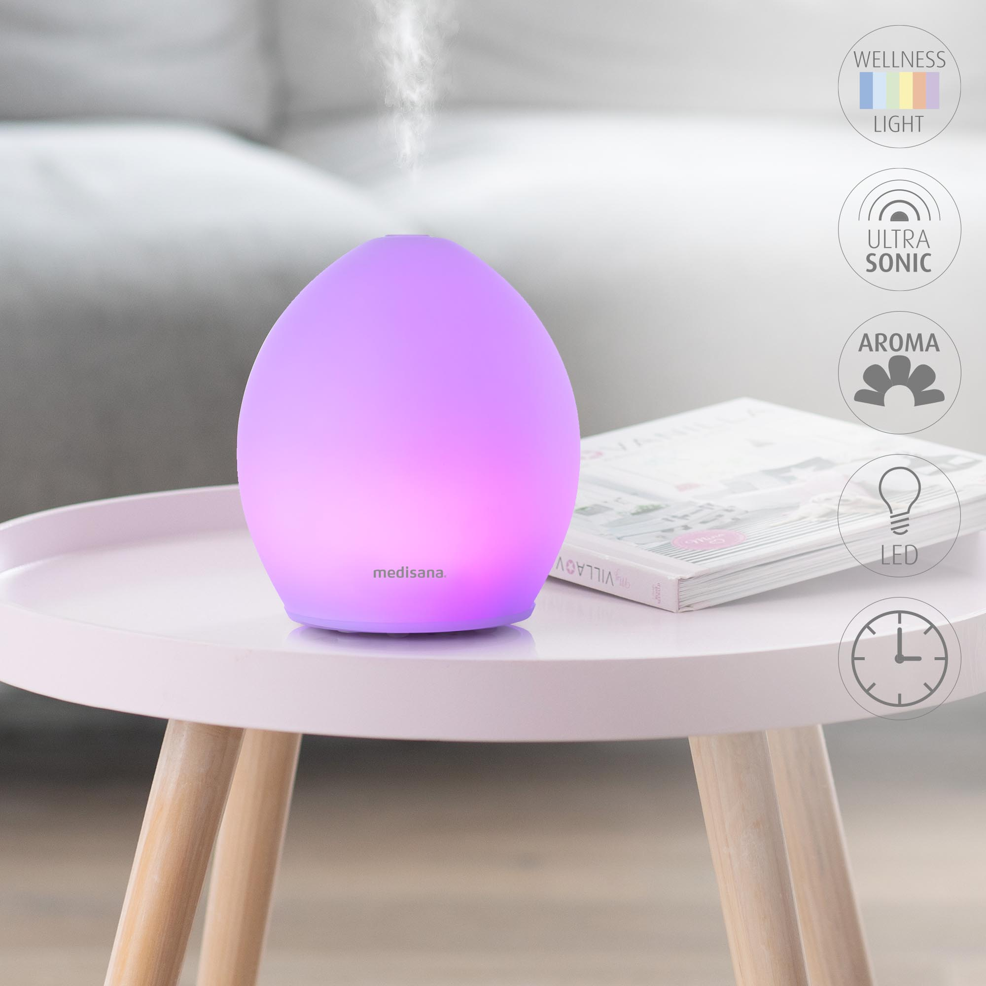 A glowing purple aroma diffuser on a pink table with a book.