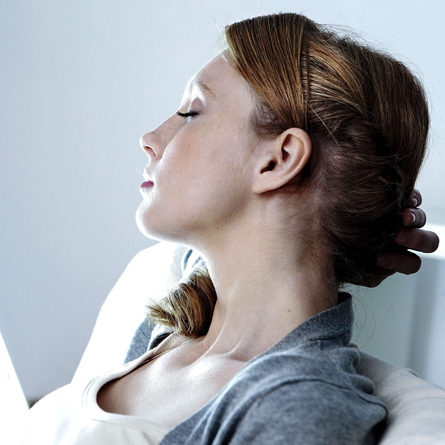 Kobieta w profilu, z zamkniętymi oczami, w szarej koszuli, ręka na głowie.