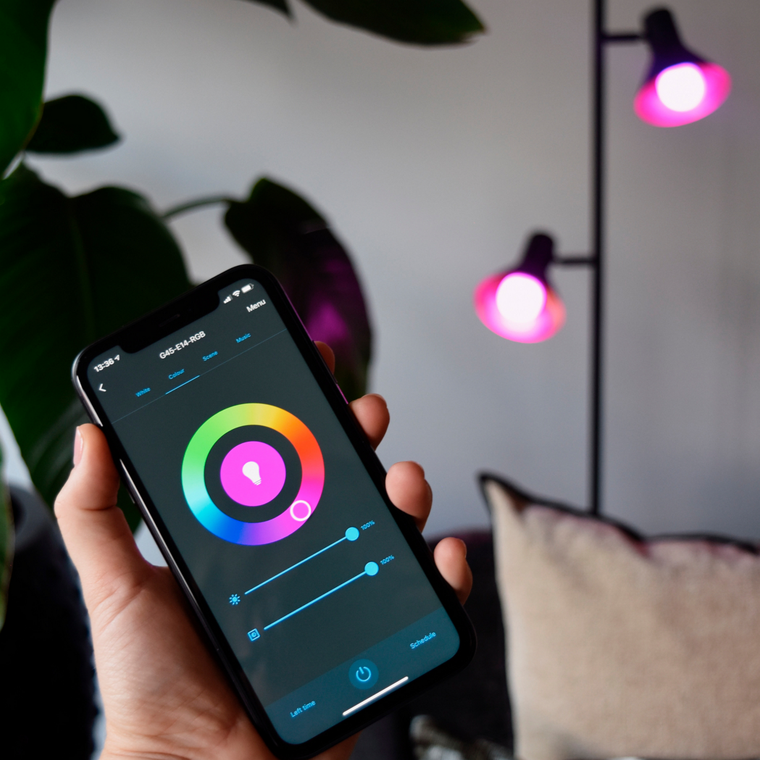 Una mano che tiene un telefono con un'app di controllo del colore, vicino a una lampada da terra.