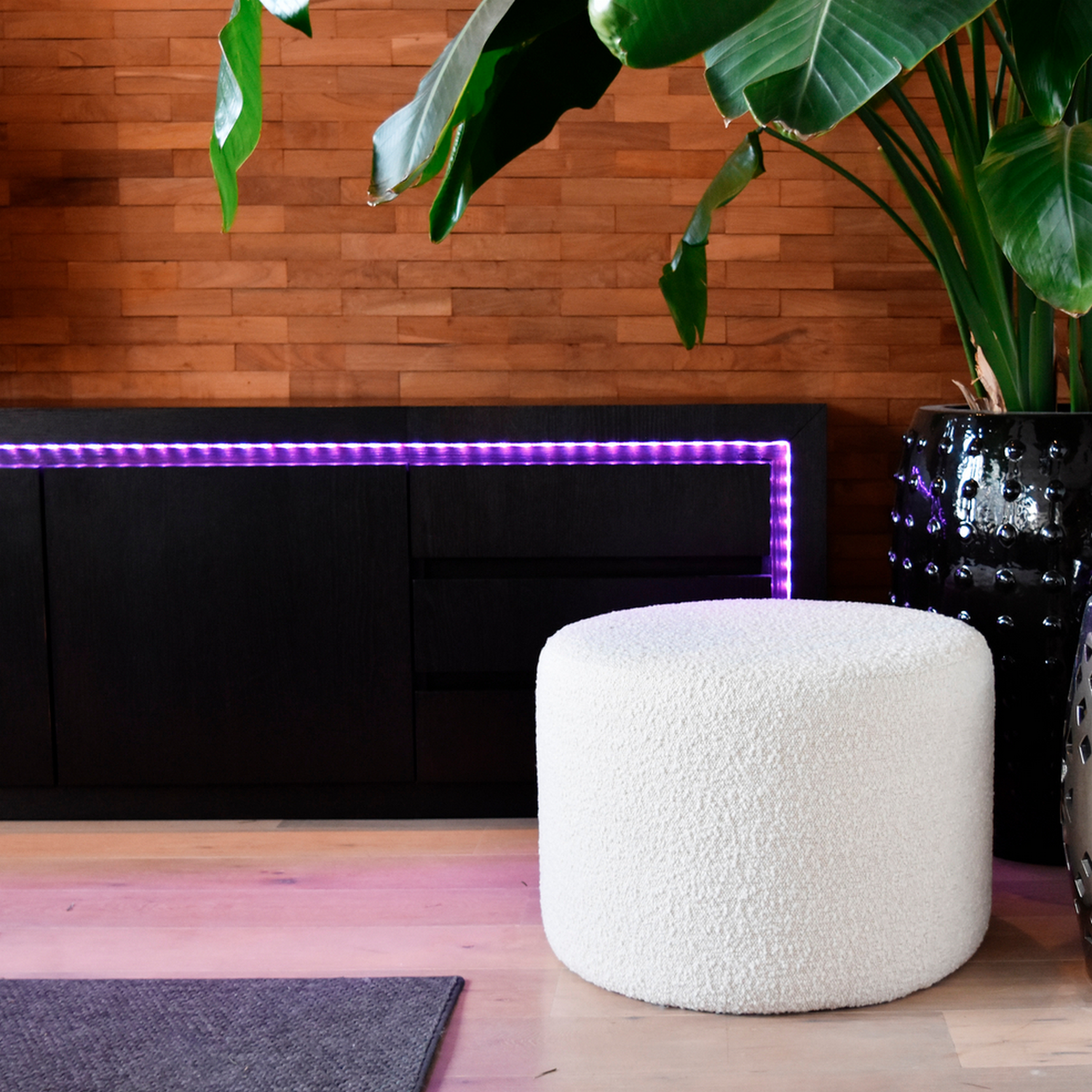 Pouf rotondo bianco in soggiorno con pannelli in legno e pianta.