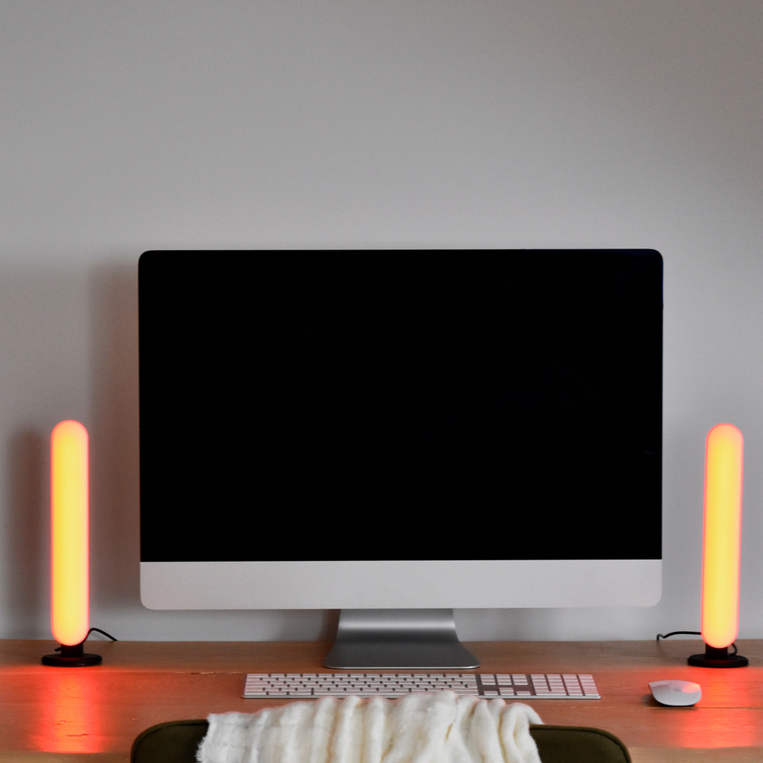 Una scrivania con un computer, una tastiera e due bastoncini luminosi a LED. C'è una coperta bianca e un mouse.