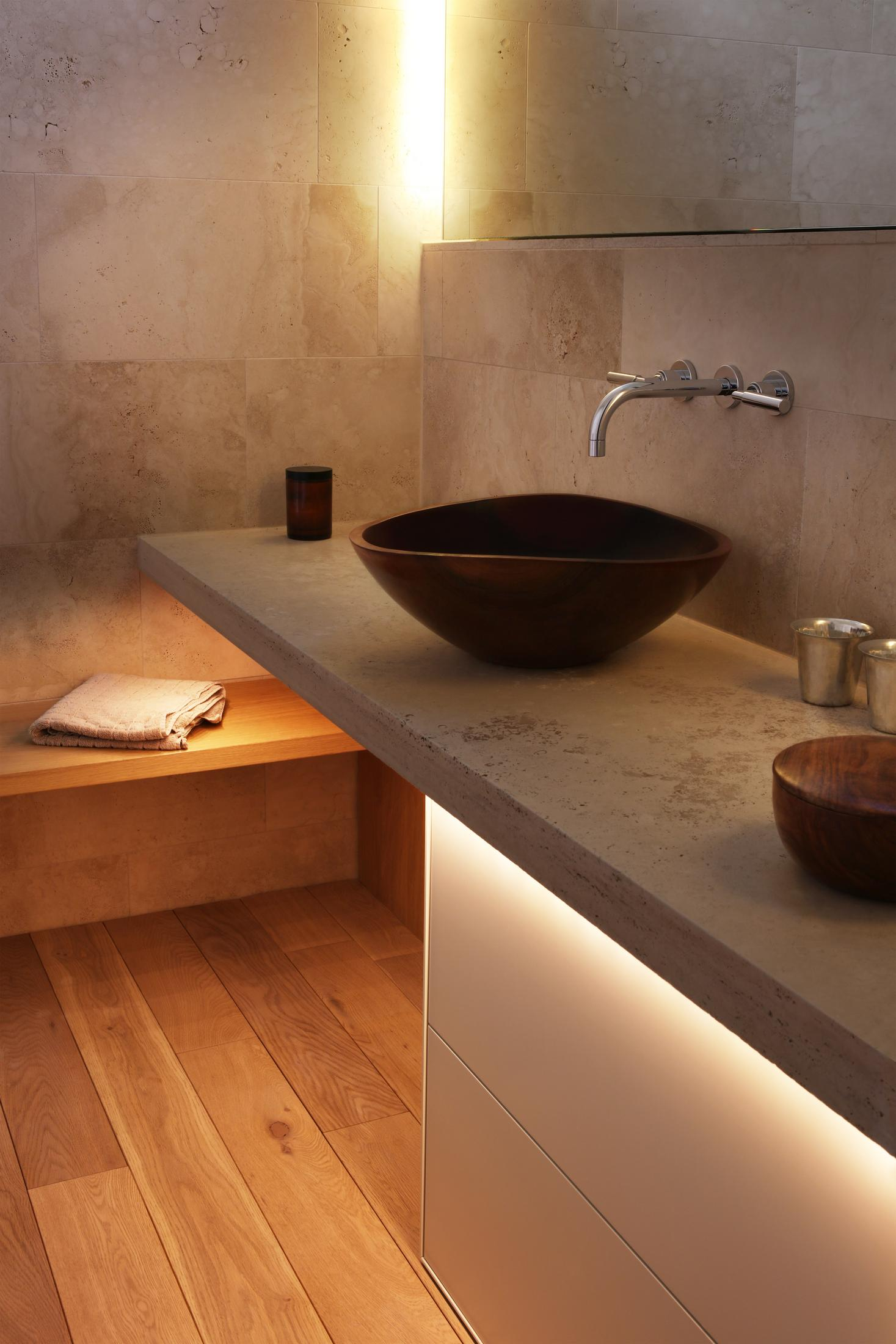 Bagno con lavabo scuro, pavimento in legno, asciugamano e mensola illuminata.