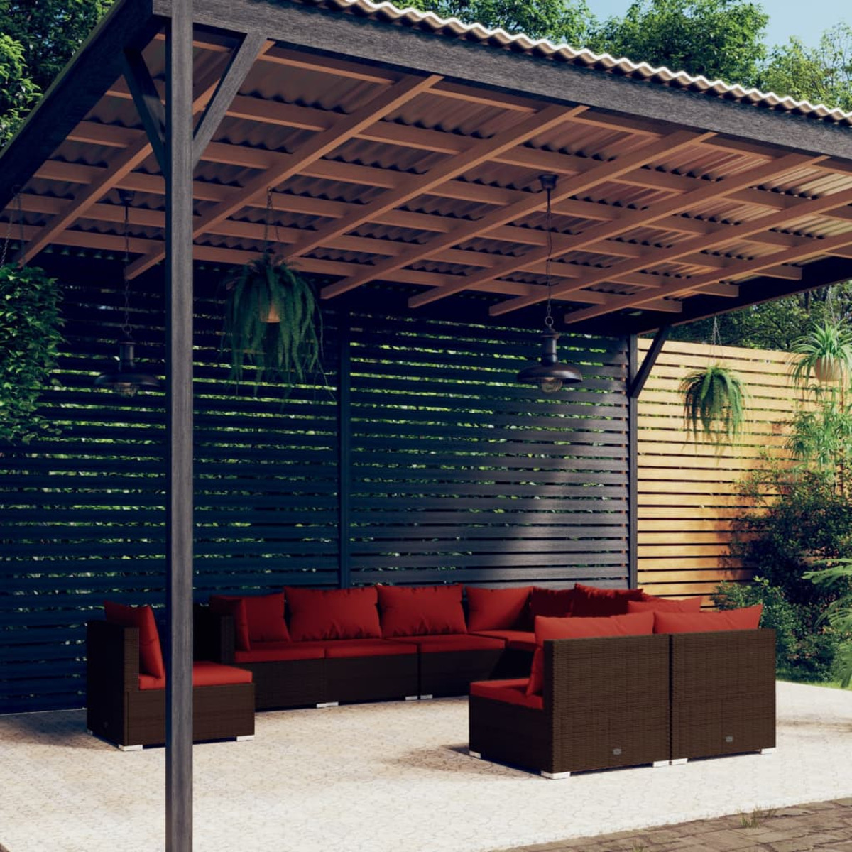 Außenbereich mit braunen Rattansitzmöbeln, roten Kissen unter einer Holzpergola. Grüne Pflanzen umgeben.