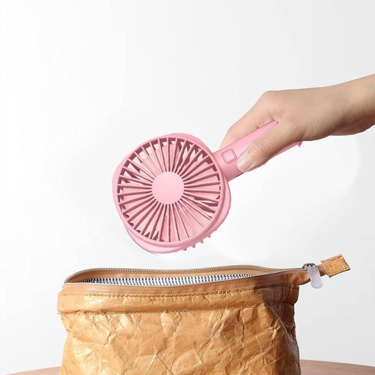 Hand, die einen rosa Ventilator über einer braunen Papiertüte hält. Der Ventilator ist offen.