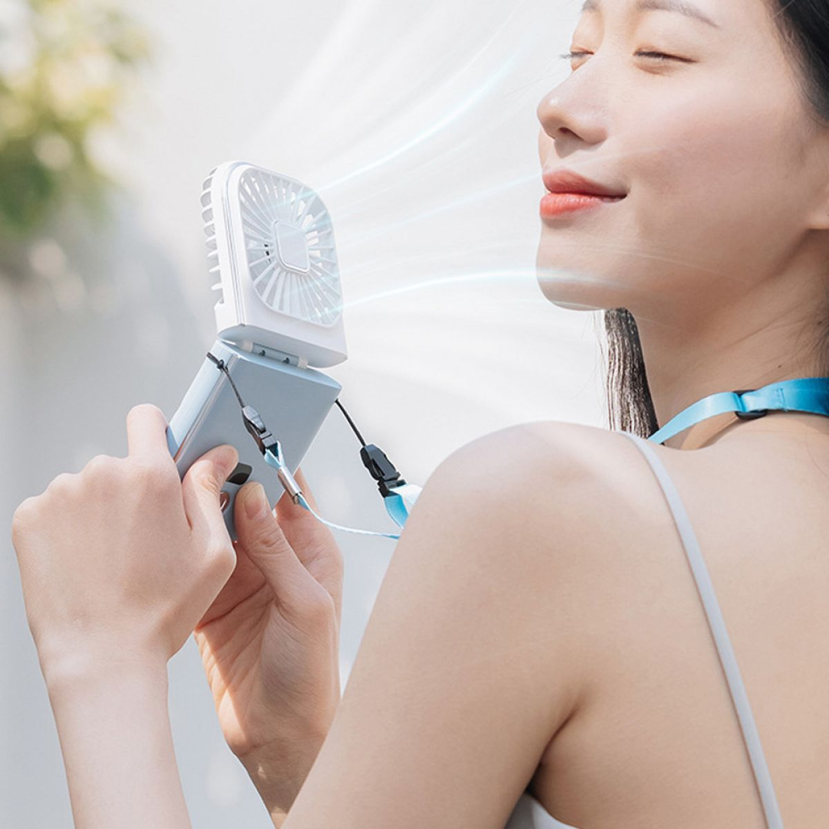 Eine Frau benutzt einen tragbaren Ventilator. Der Ventilator ist weiß und blau, und sie hält ihn.