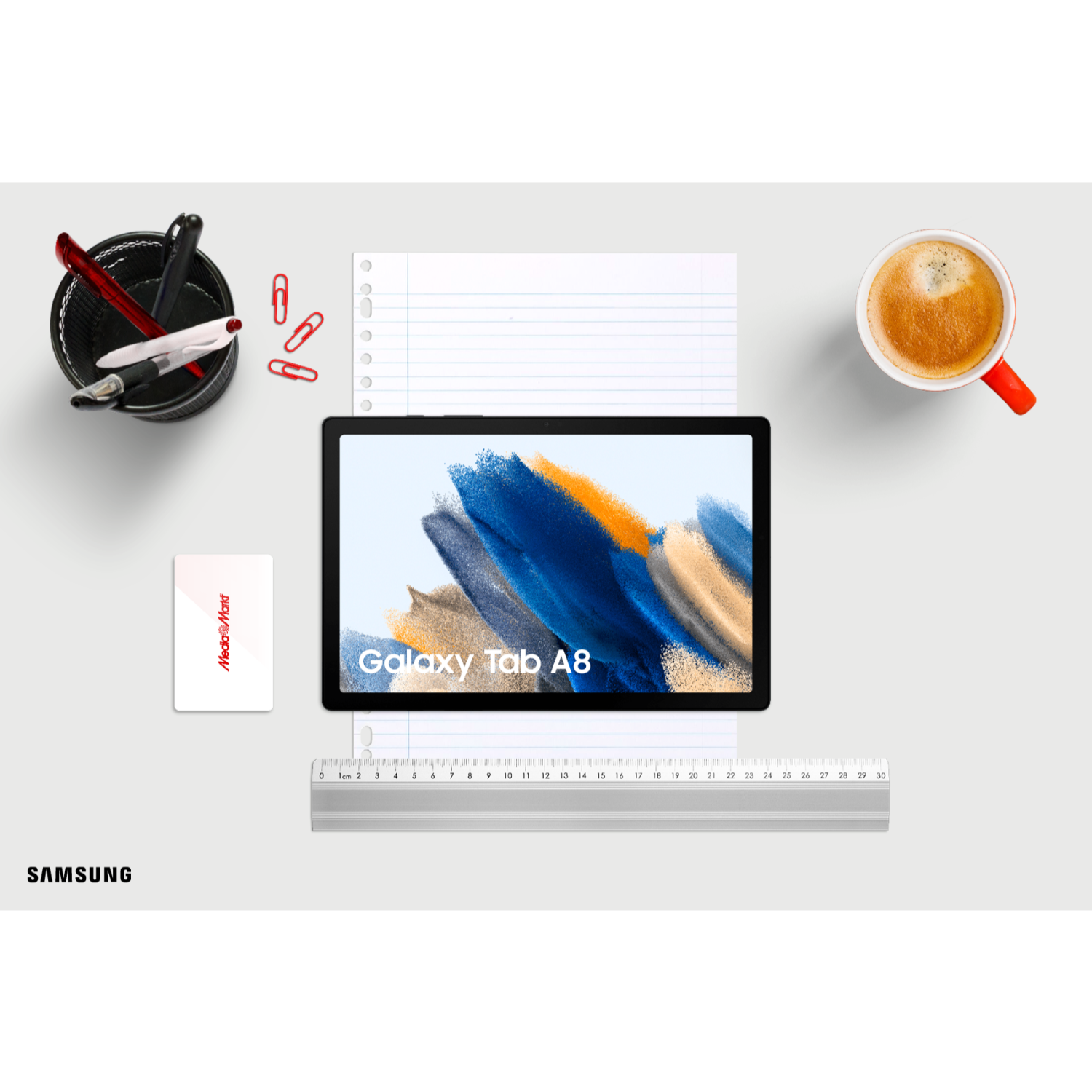 Een tablet op een bureau met schrijfwaren, koffie en een rode Mediamarkt-kaart.