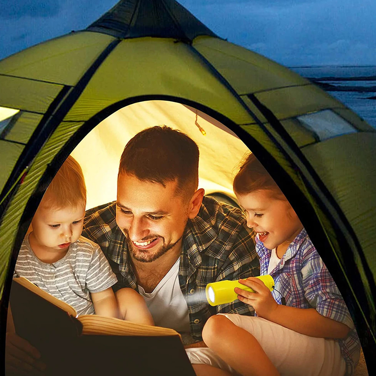 Eine Familie in einem Zelt, liest ein Buch mit einer Taschenlampe bei Nacht.