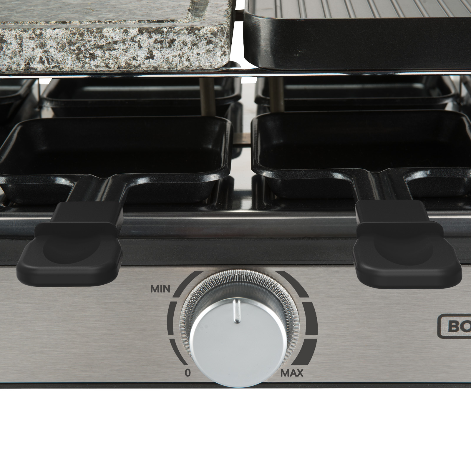 Primer plano de una parrilla de raclette con dial de control y sartenes negras.