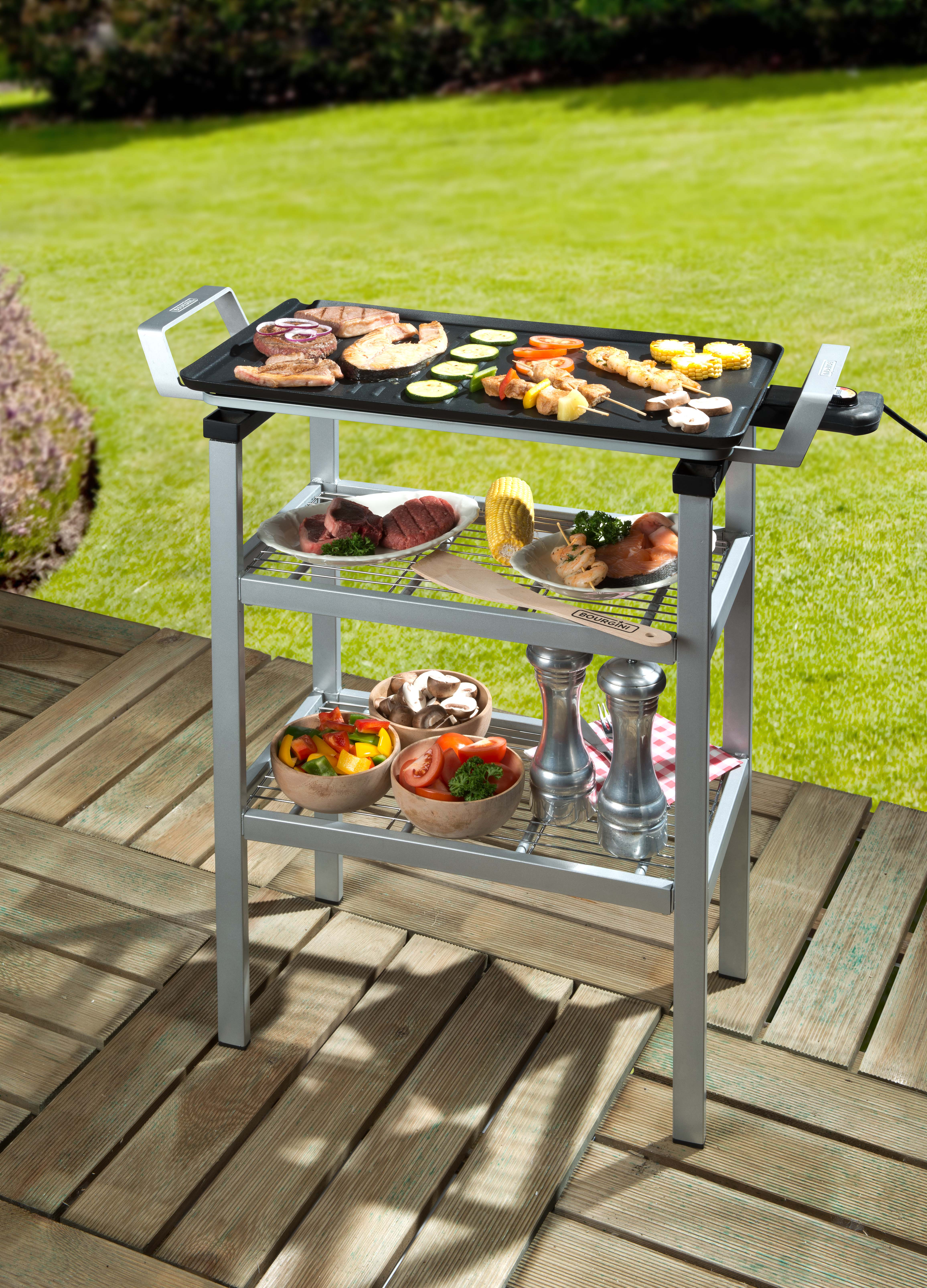 Elektrischer Grill mit gekochtem Essen, Regalen mit Essen und Gartenhintergrund.