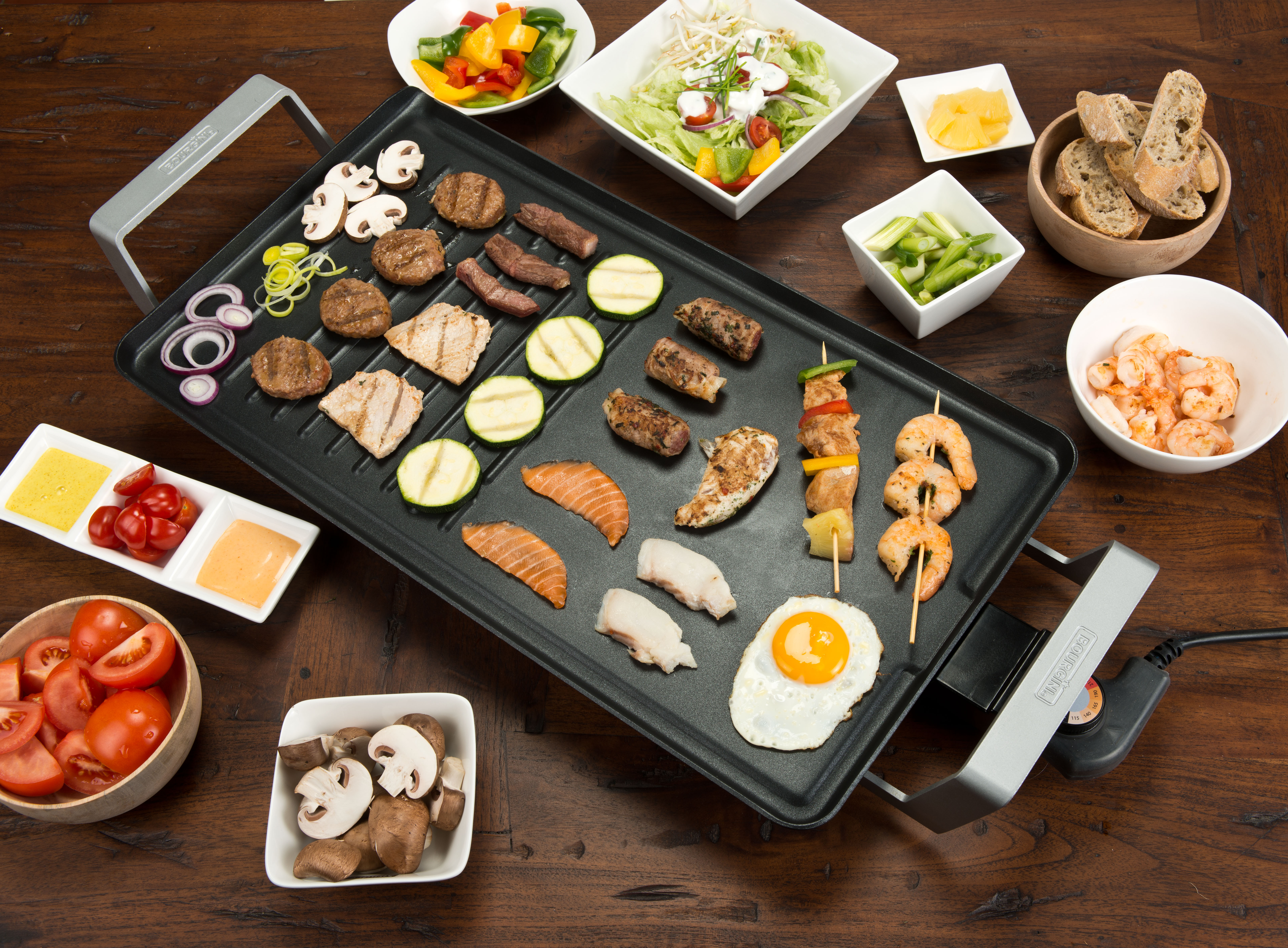 Ein Grill mit gekochtem Essen, darunter Fleisch, Gemüse und Meeresfrüchte. Verschiedene Beilagen sind vorhanden.