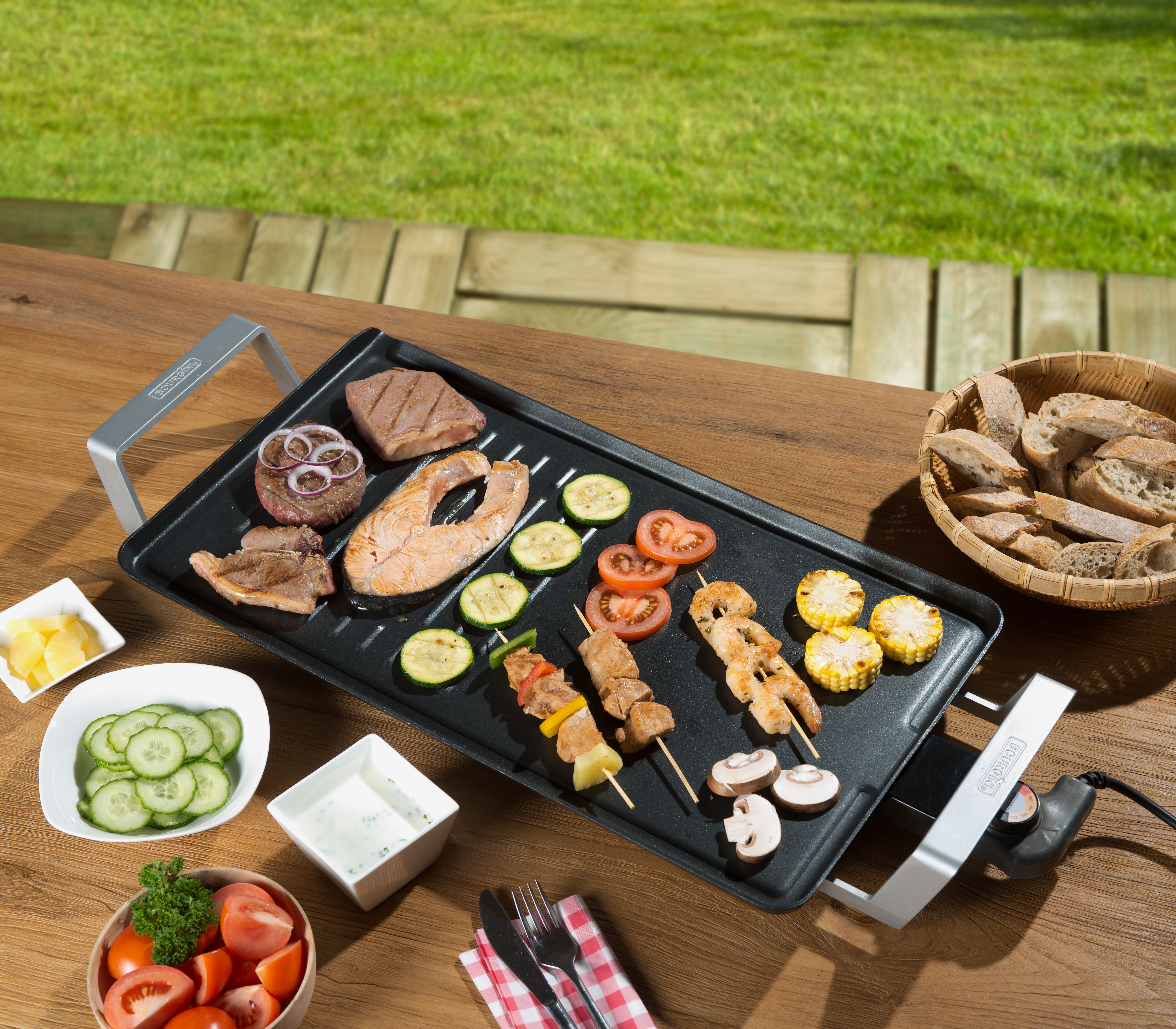 Grill mit gekochtem Essen: Burger, Lachs, Gemüse und Spieße. Serviert mit Beilagen und von Gras umgeben.