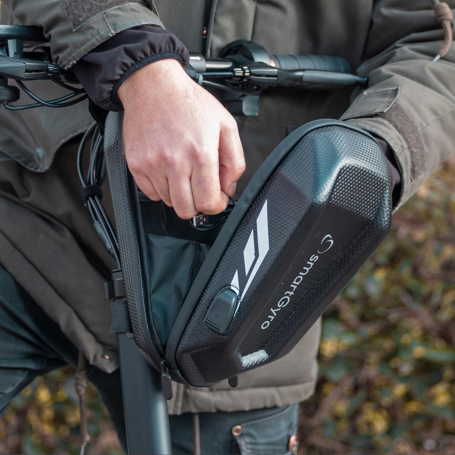 Osoba otwierająca czarną torbę przymocowaną do skutera. Torba ma zamek błyskawiczny.