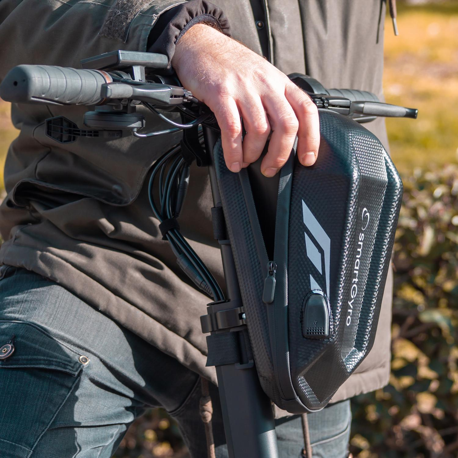 Dłoń trzyma czarną torbę SmartGyro przymocowaną do kierownicy hulajnogi elektrycznej.