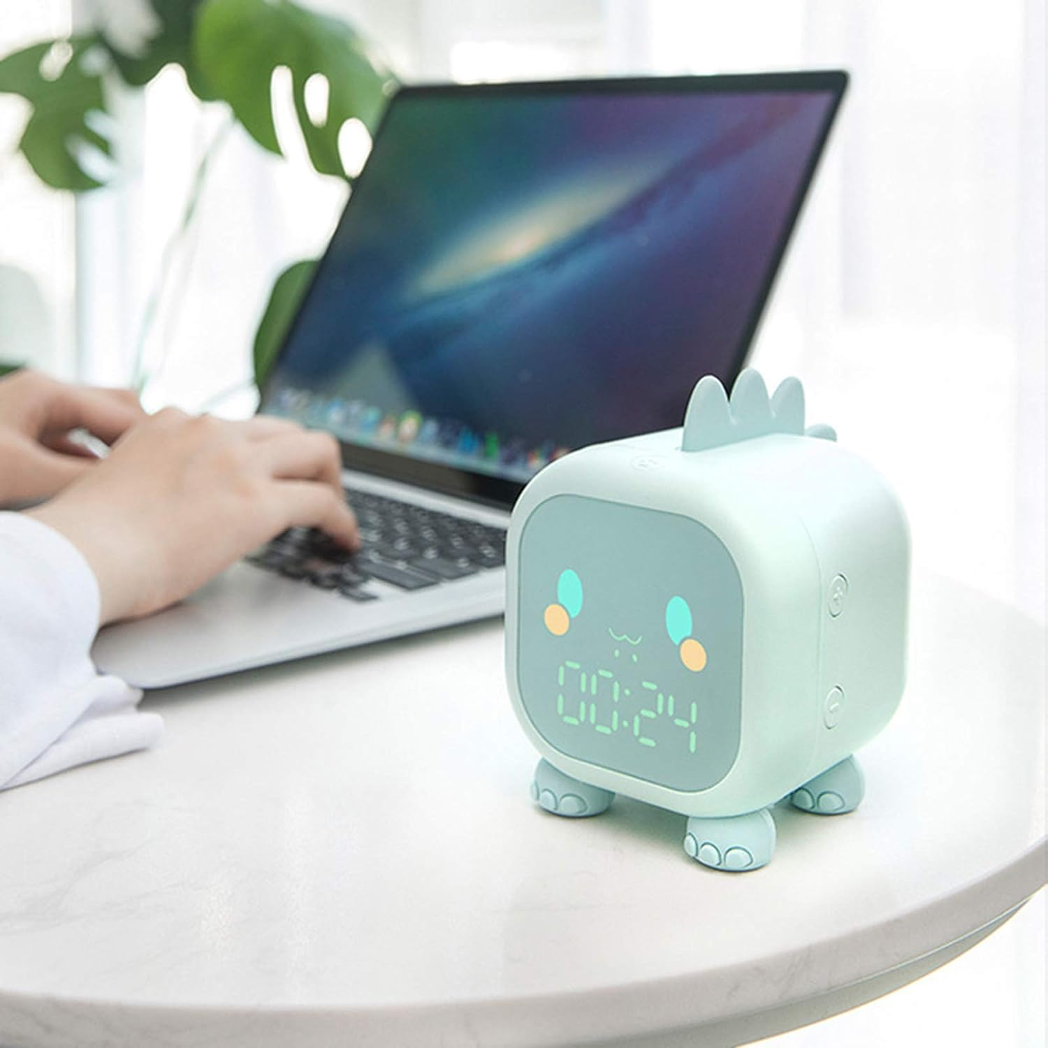 Dinosaurierförmige Digitaluhr auf einem Tisch. Im Hintergrund arbeitet eine Person am Laptop.