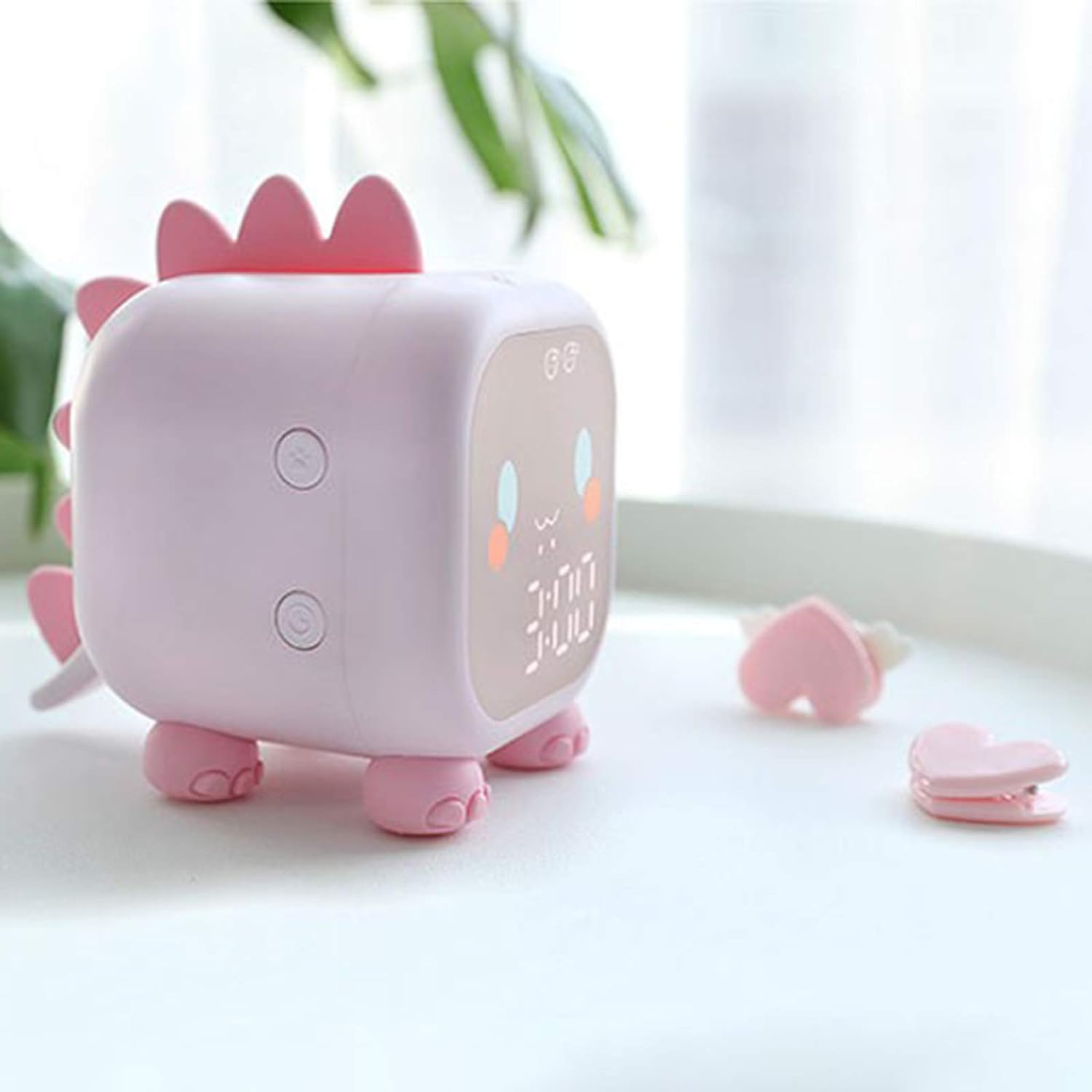 Rosa dinosaurierförmiger Wecker mit Digitalanzeige. Rosa Herzen liegen verstreut in der Nähe.