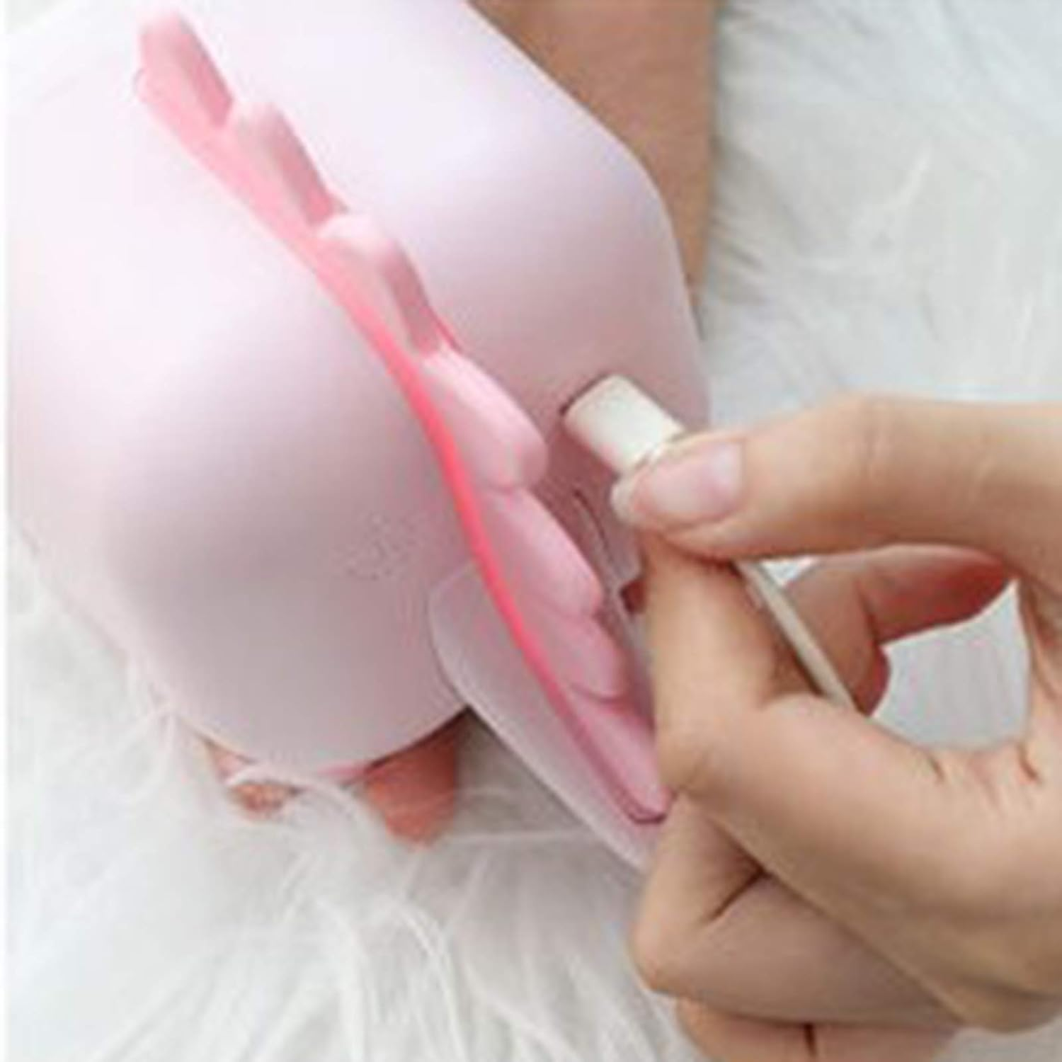 Eine Hand steckt das Ladegerät in ein rosa Gerät mit flügelartigen Formen auf flauschiger Oberfläche.