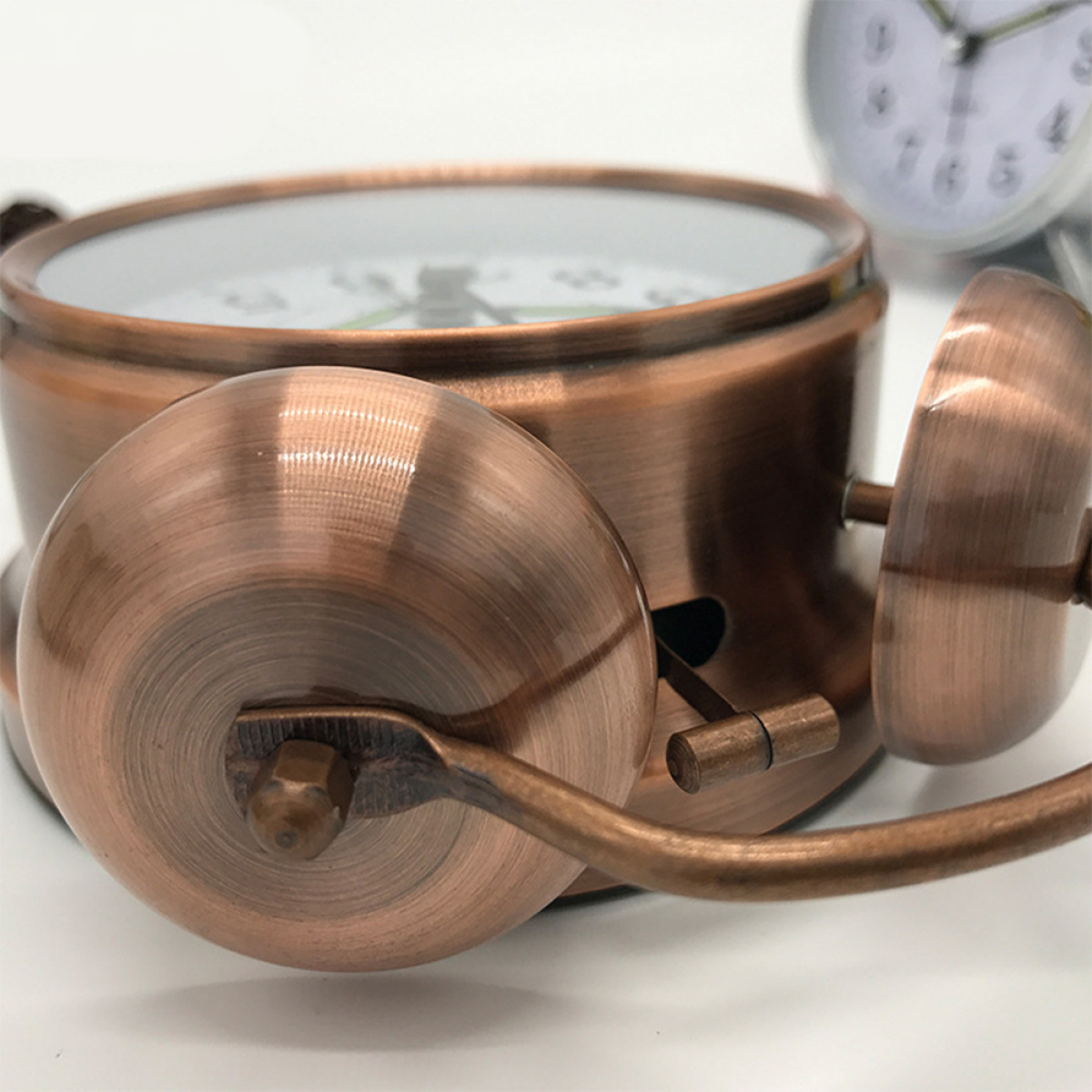 Antiker Kupfer-Wecker mit Details der Glocke und des Zifferblatts, vor weißem Hintergrund.