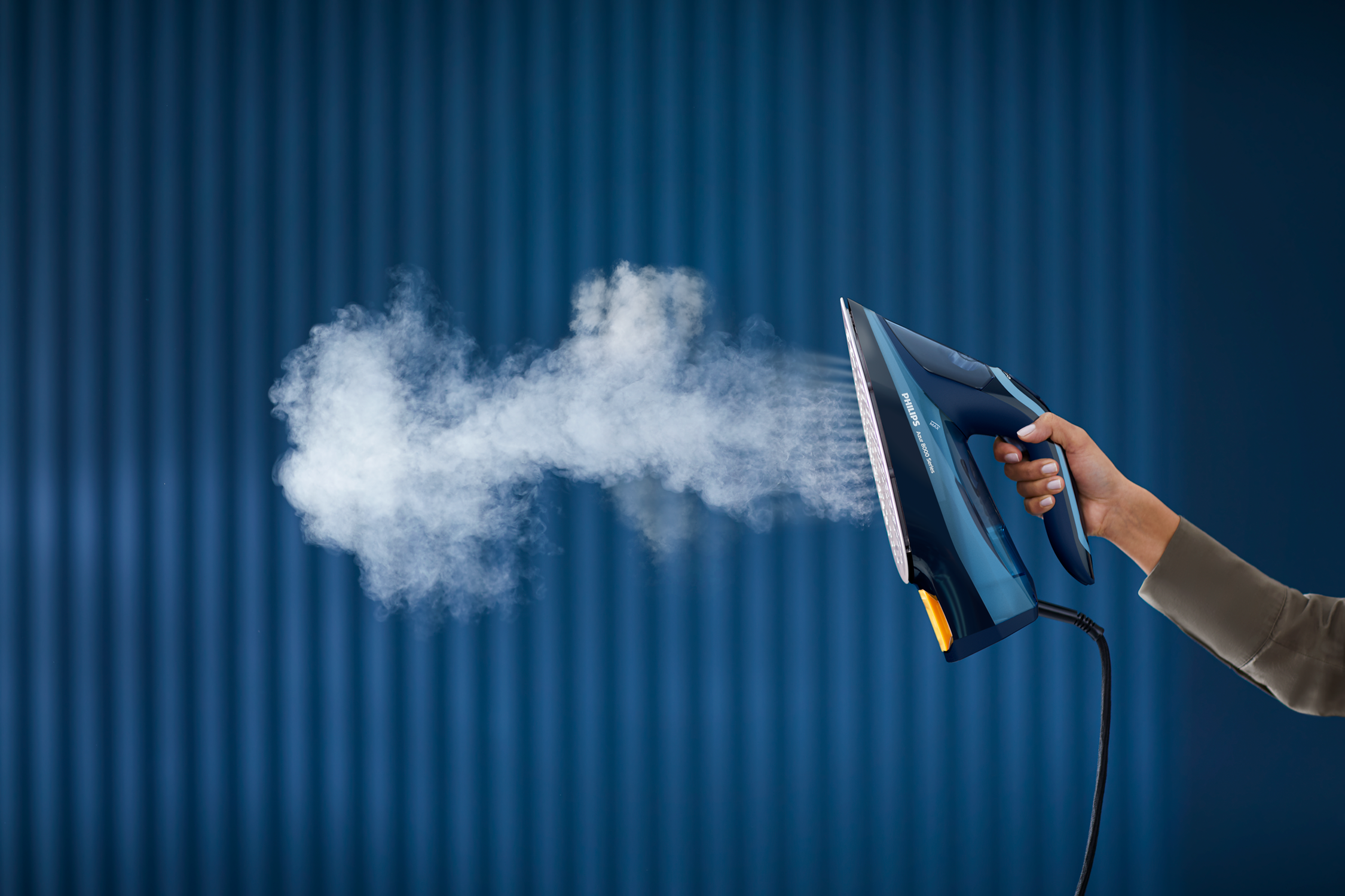 Żelazko parowe. Para wydobywająca się z żelazka. Niebieskie tło ściany.