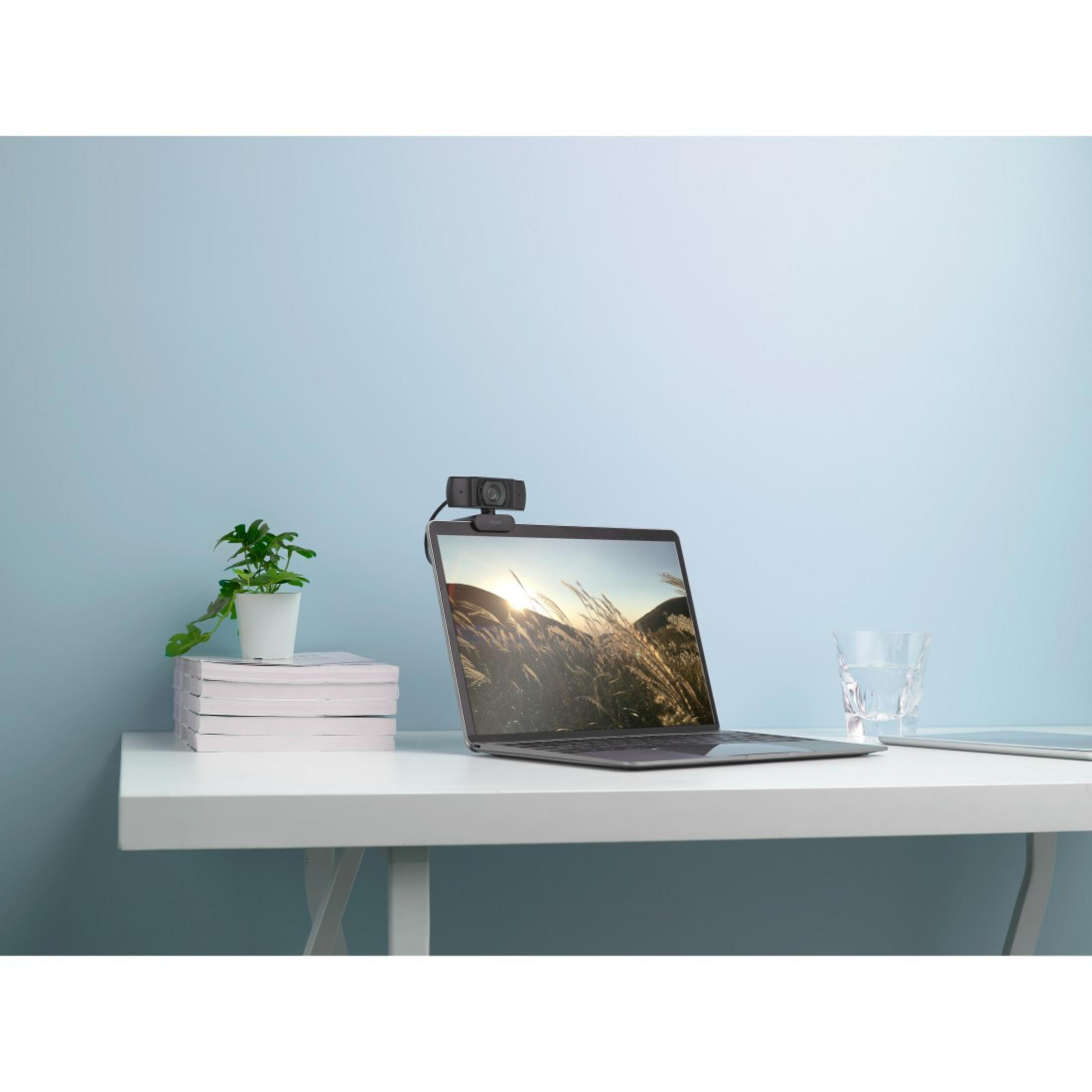 Laptop z kamerą internetową zamontowaną na górze, na białym biurku. Roślina i szklanka.