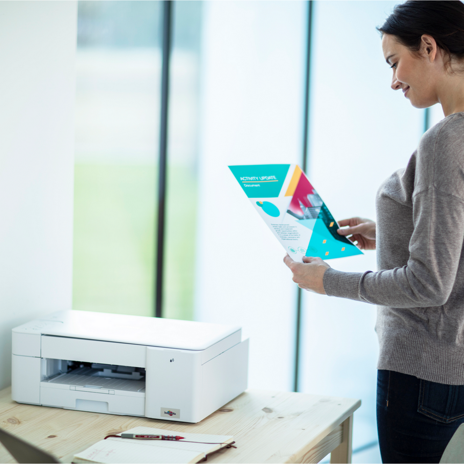 Kobieta przegląda dokument, obok drukarki. Biała drukarka na drewnianym stole.