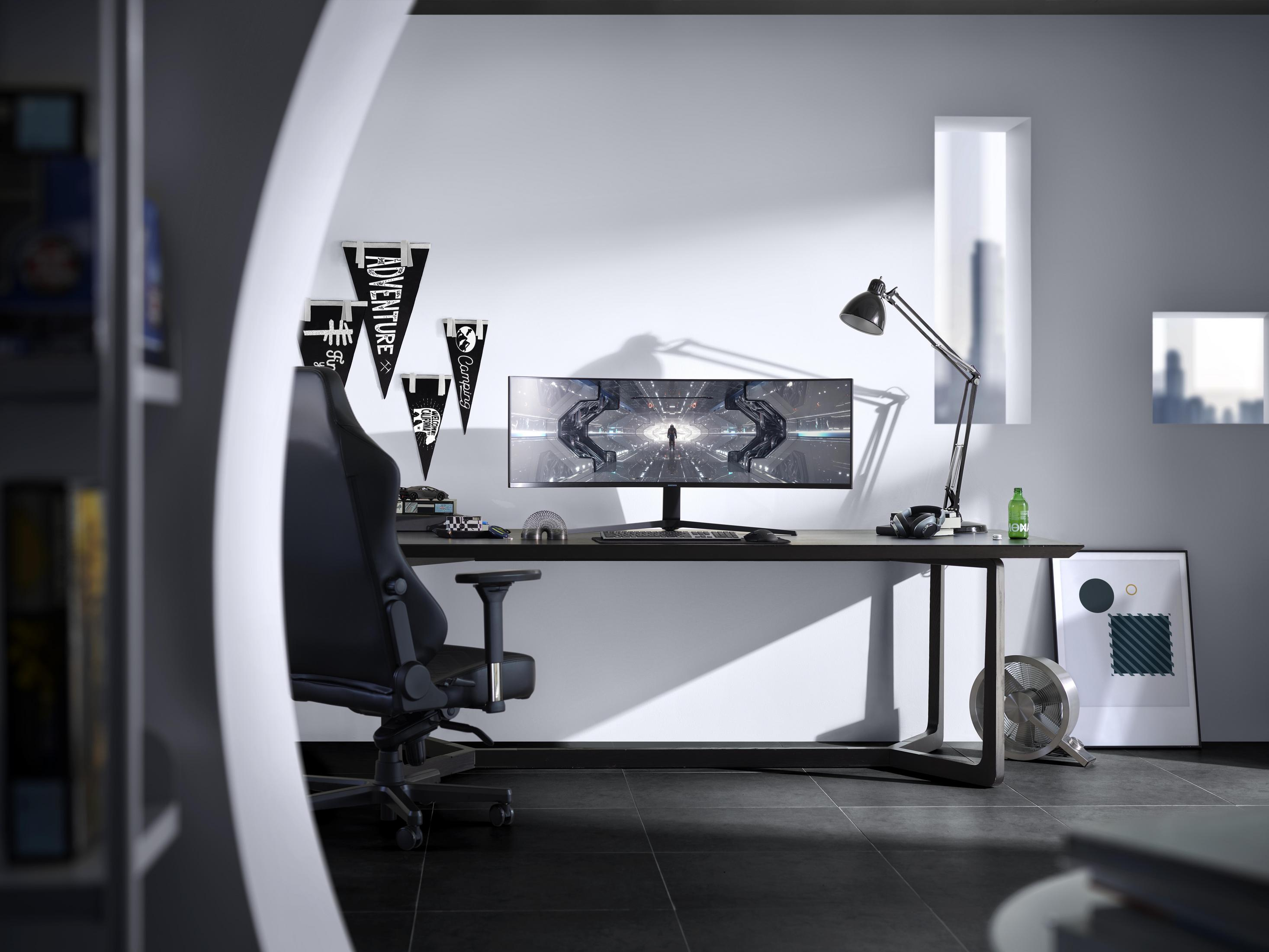 Scrivania con monitor, sedia e decorazioni. Una finestra sullo sfondo, con vista città.
