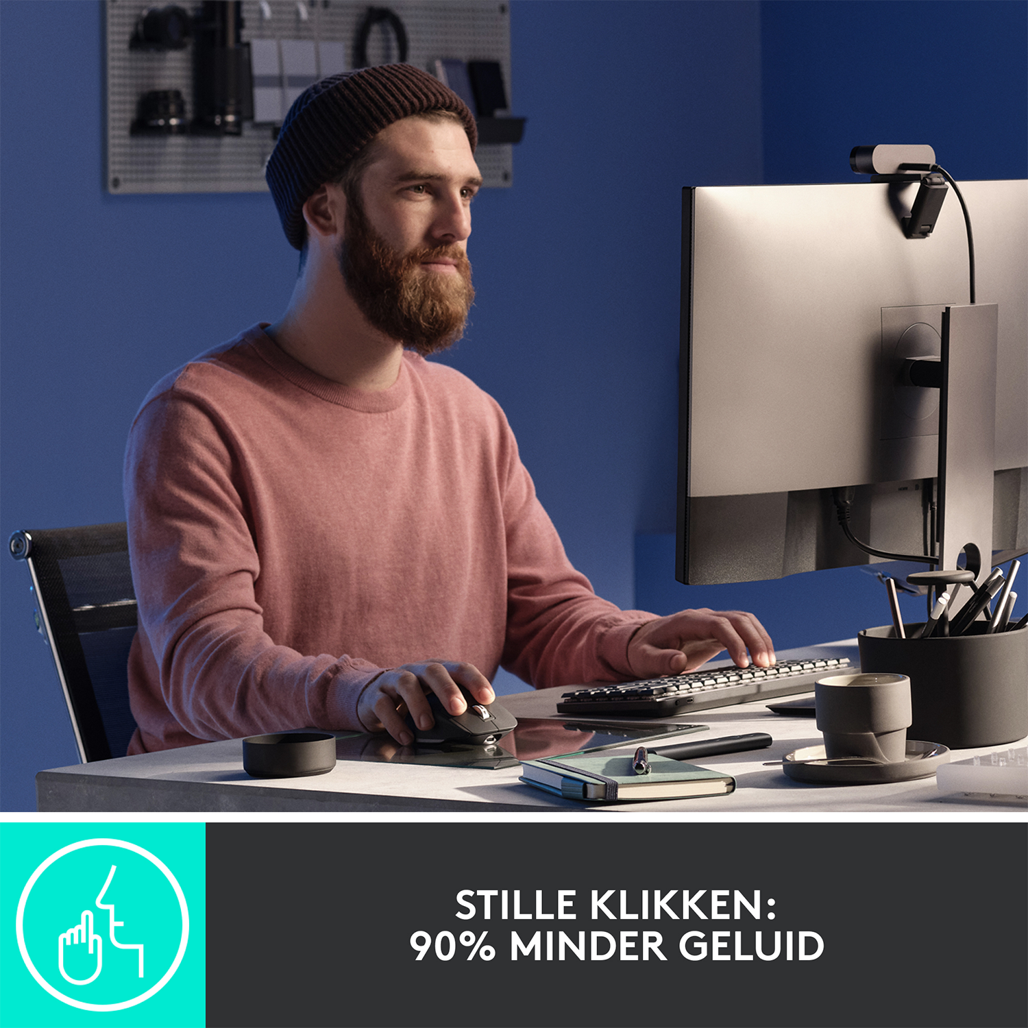 Mężczyzna korzystający z komputera. Siedzi przy biurku z monitorem, klawiaturą, myszą i kamerą internetową.