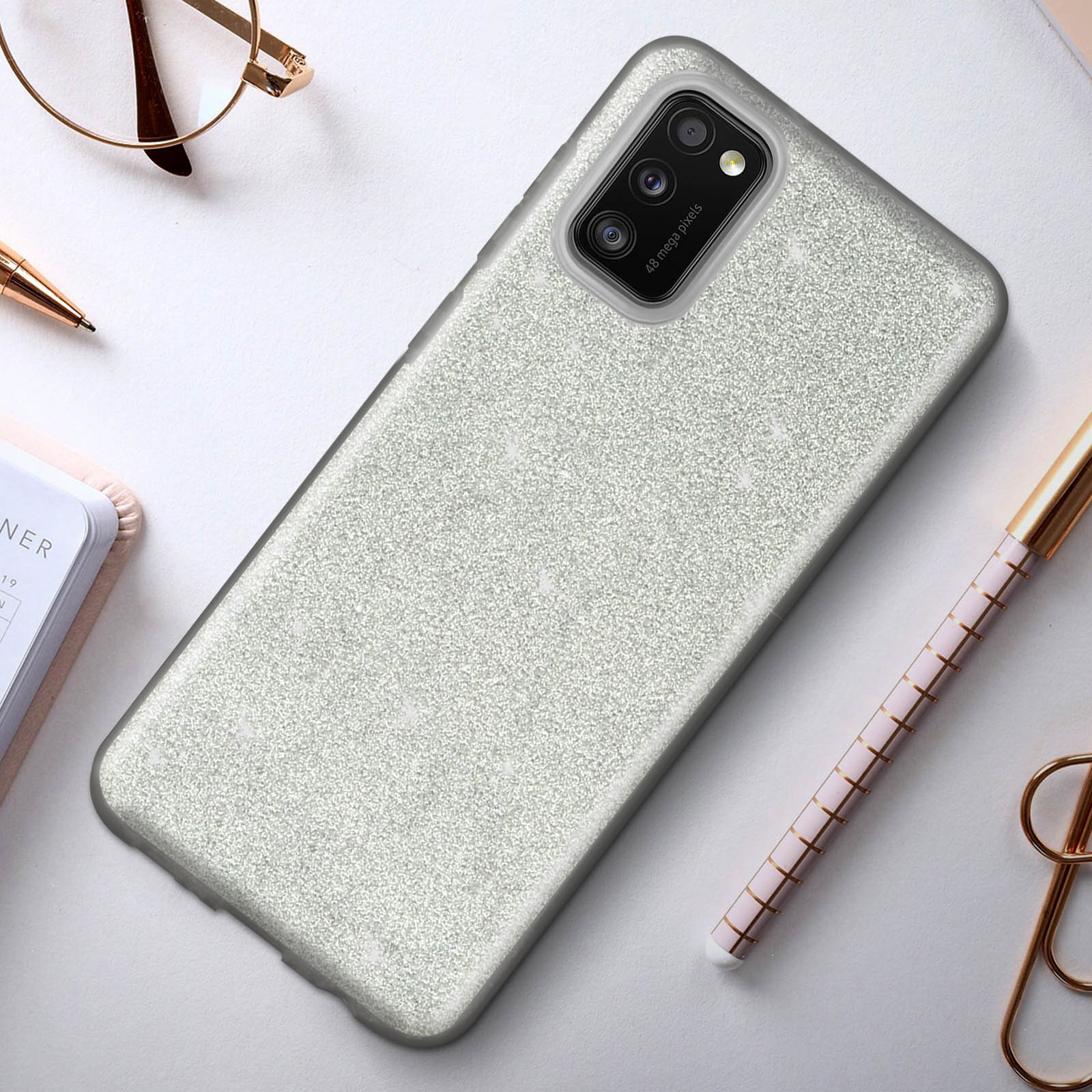 Glitterende zilveren telefoonhoes op een bureau met pen, bril en notitieboek.