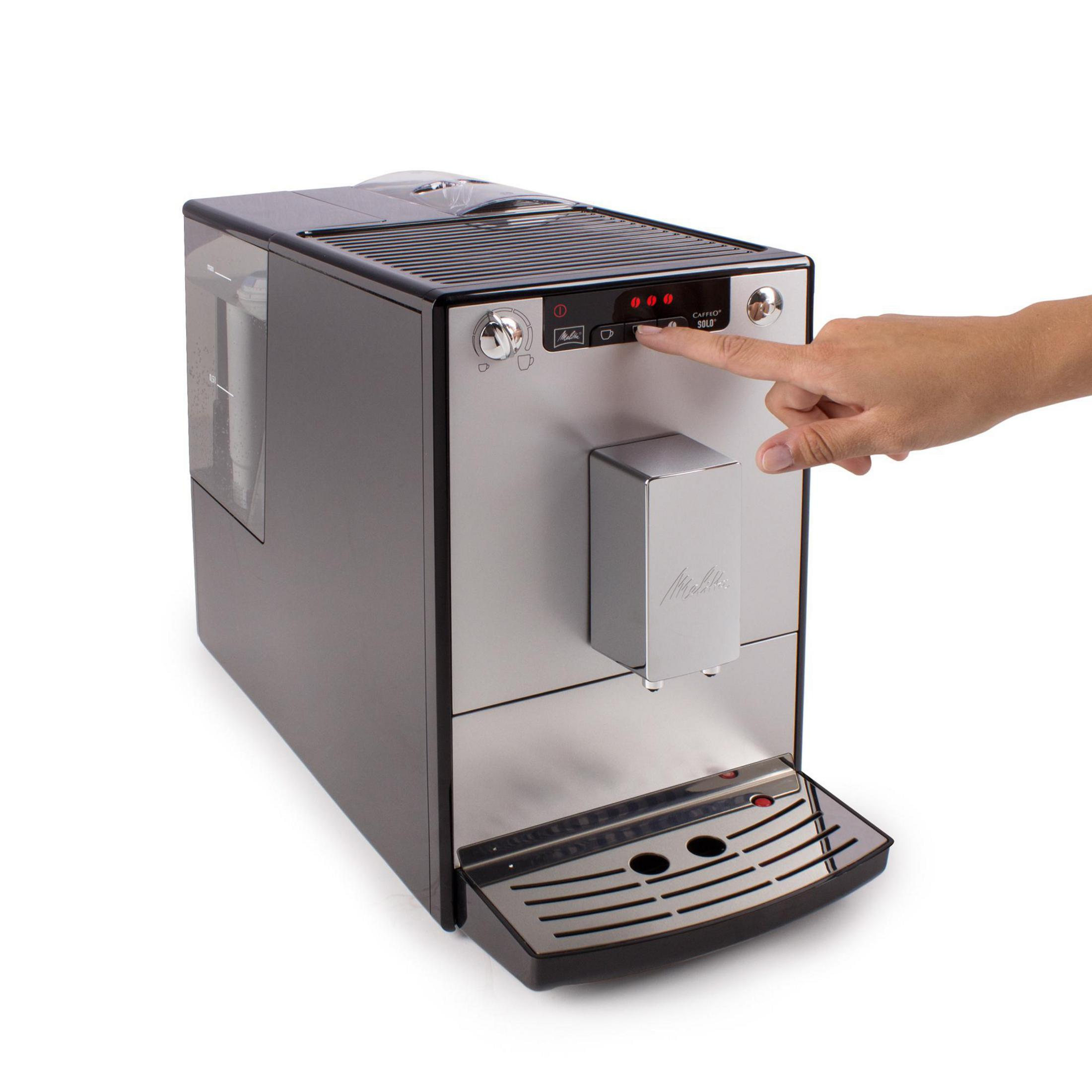 Srebrno-czarny ekspres do kawy Melitta. Ręka naciska przycisk na przednim panelu.