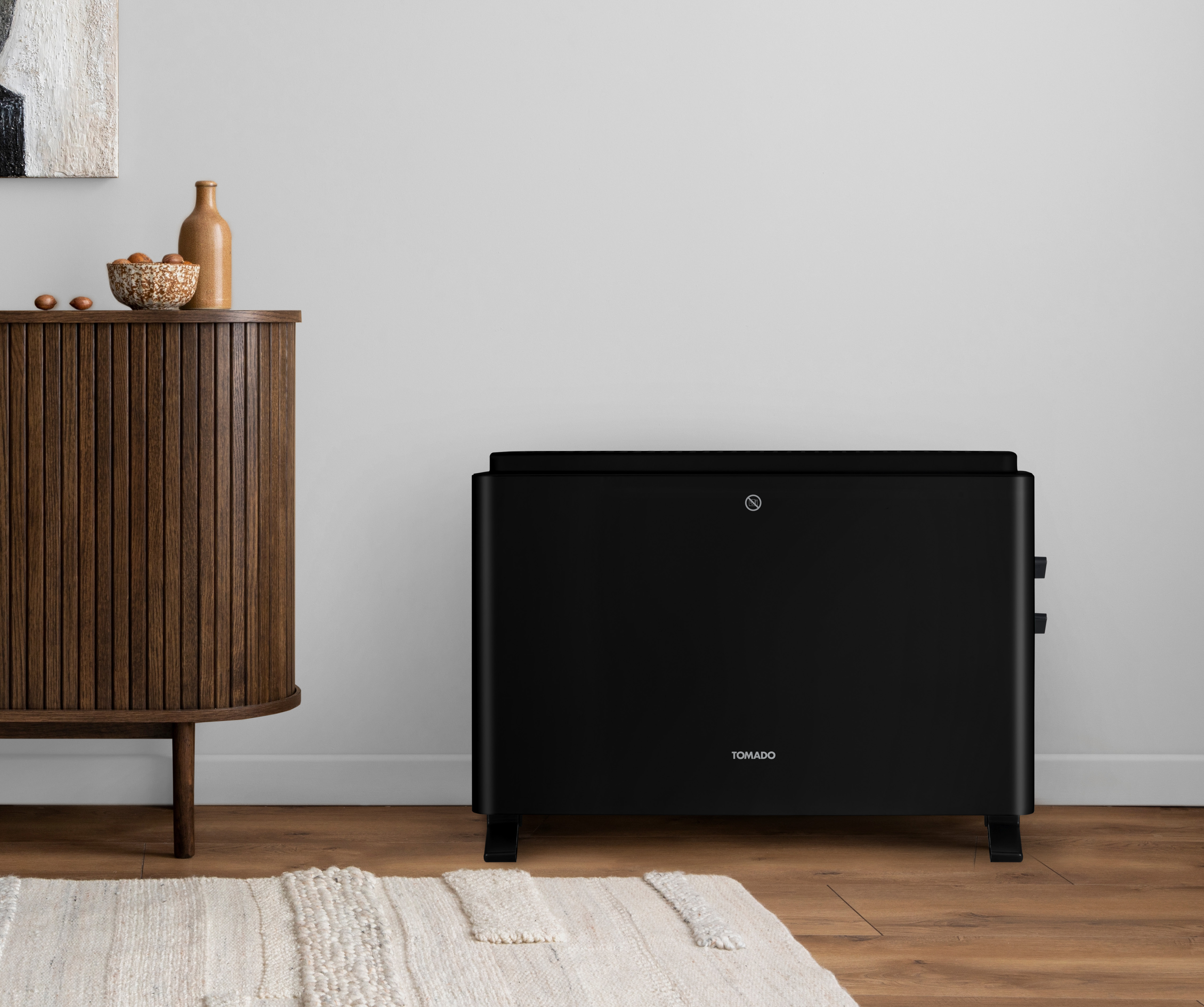 Ein schwarzer Heizkörper in einem Raum mit einem Holzschrank, weißer Wand und einem Teppich auf dem Boden.