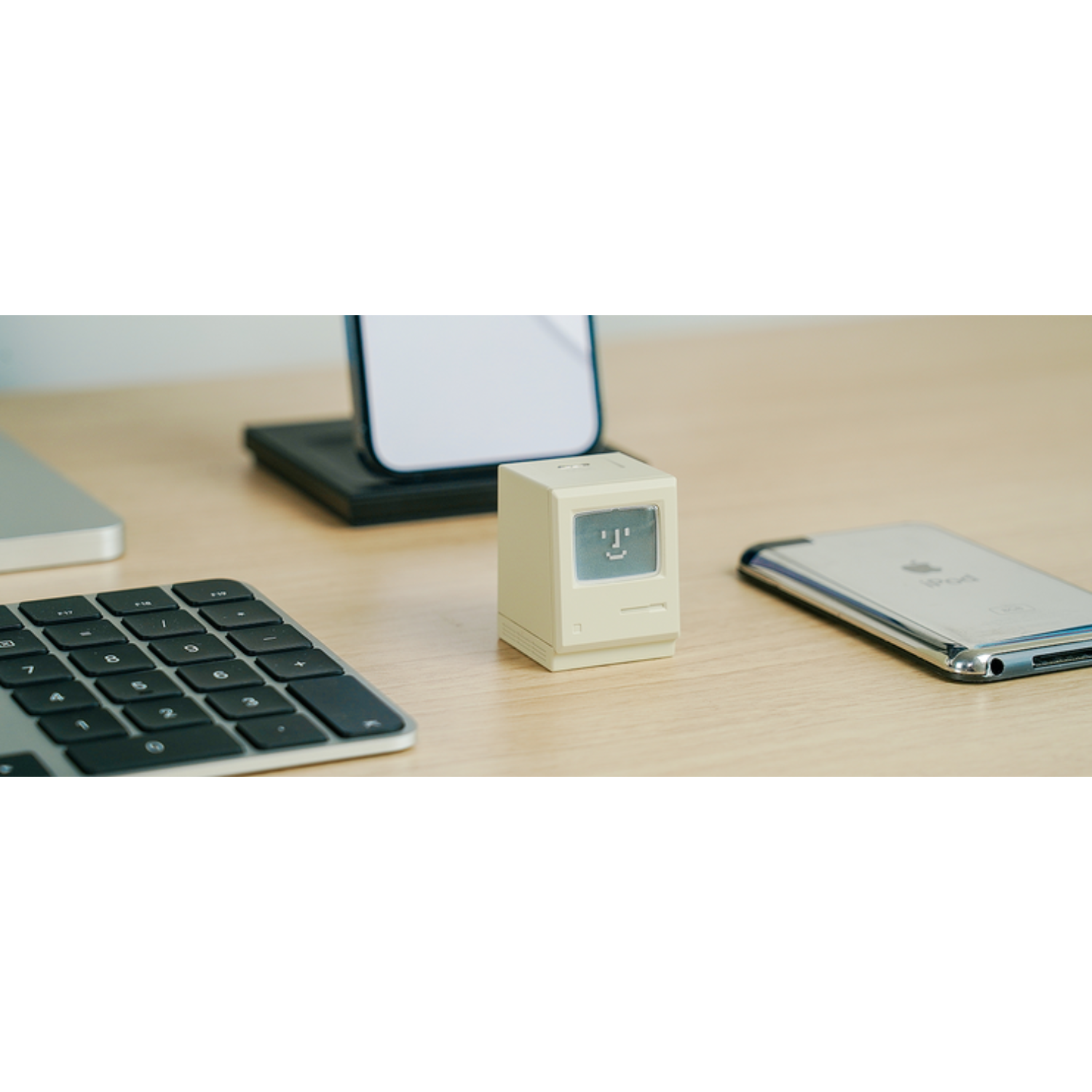 Un piccolo computer retrò su una scrivania con un iPod, una tastiera e un telefono.