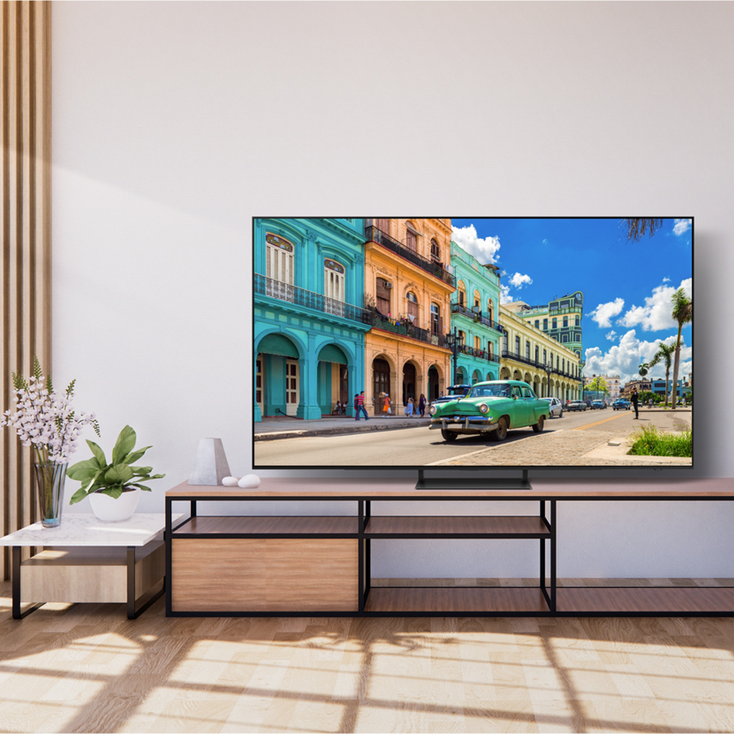 Telewizor wyświetlający kolorową scenę uliczną, zamontowany na drewnianej szafce. Pokój z jasnymi podłogami.