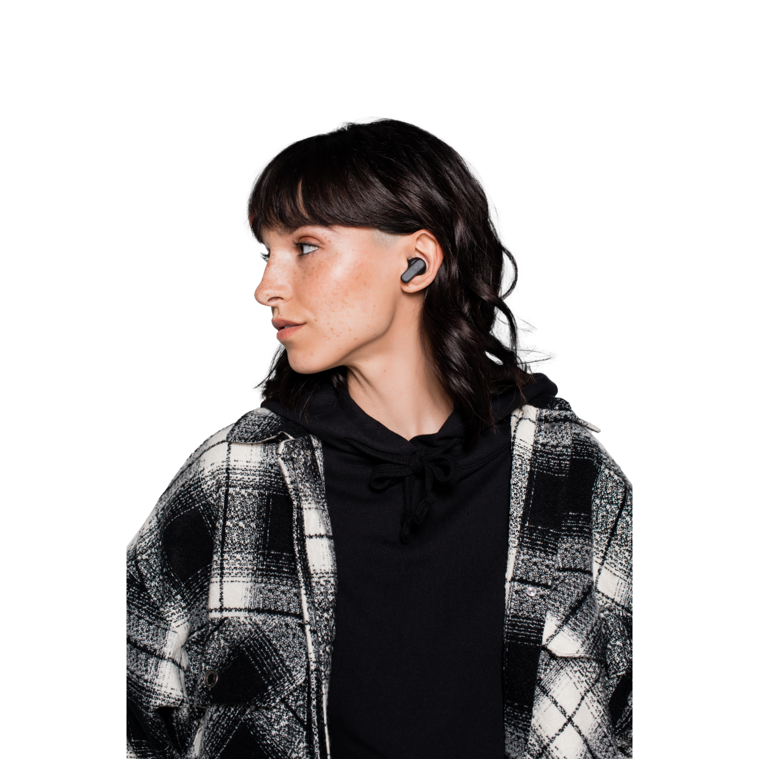 Kobieta w słuchawkach, czarnej bluzie z kapturem i koszuli w kratę, patrząca w bok na czarno-białym tle.