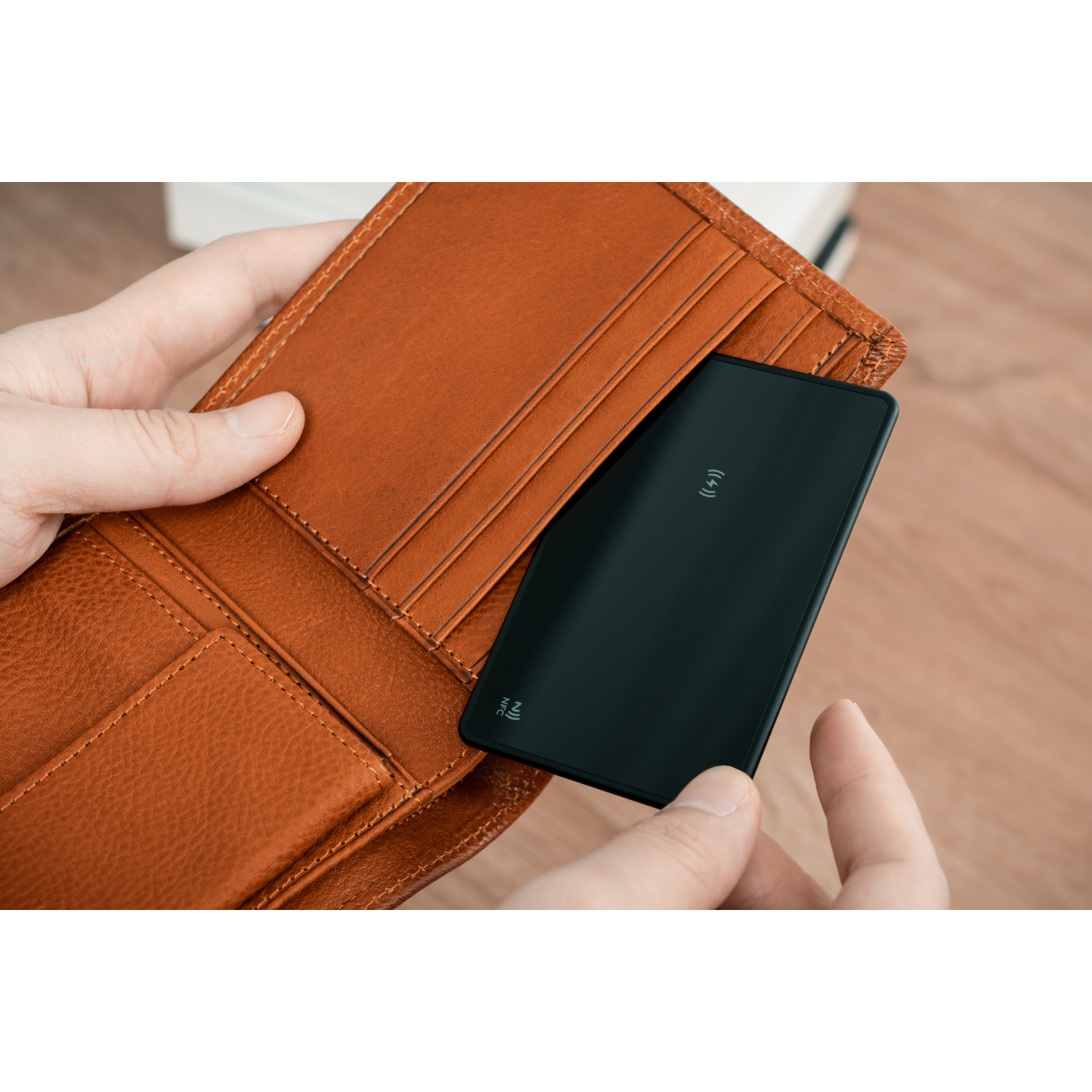 Person holding a brown leather wallet with a black card inside. Wooden surface in the background.
