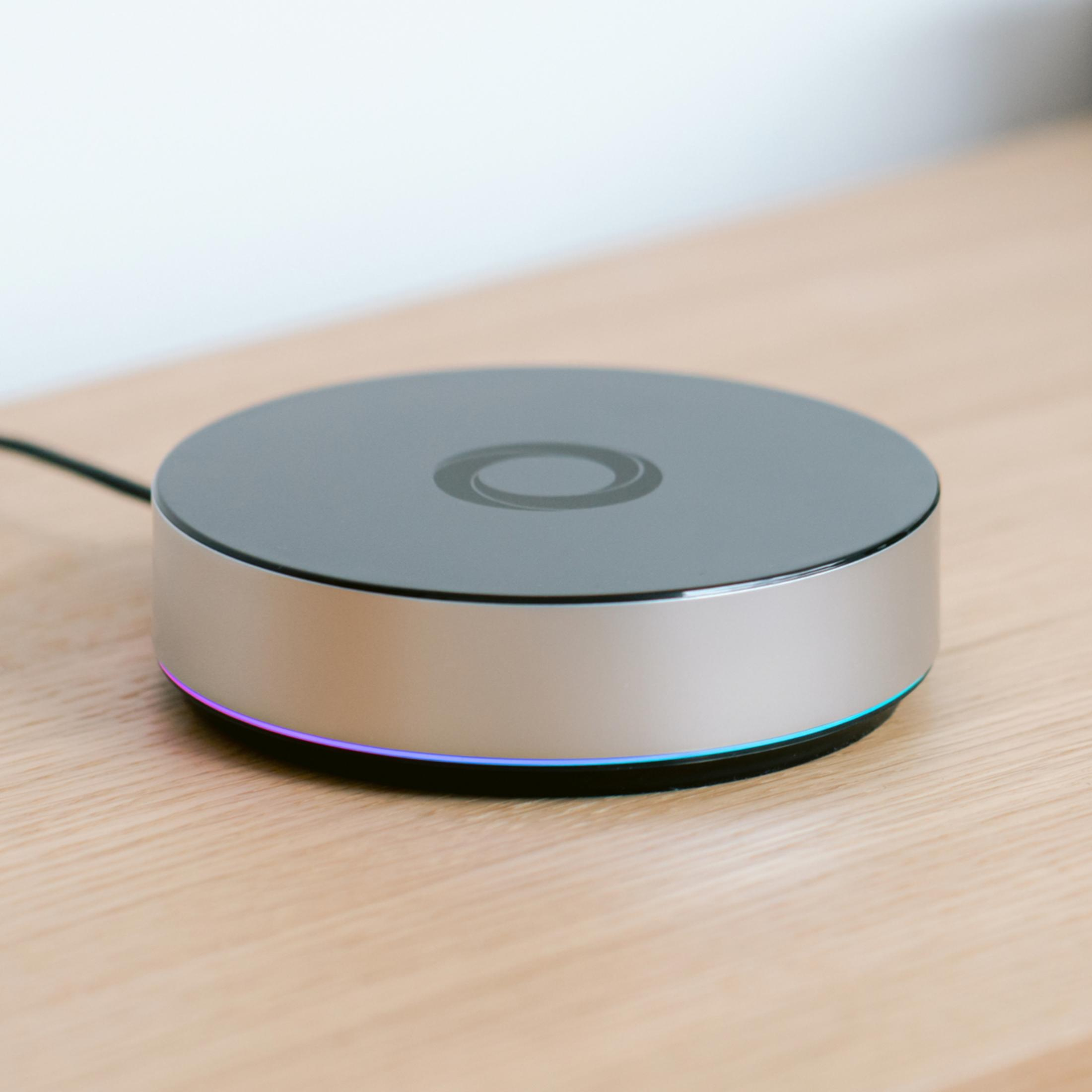Silbernes und schwarzes Smart-Home-Gerät auf einem Holztisch. Hintergrund: weiß.