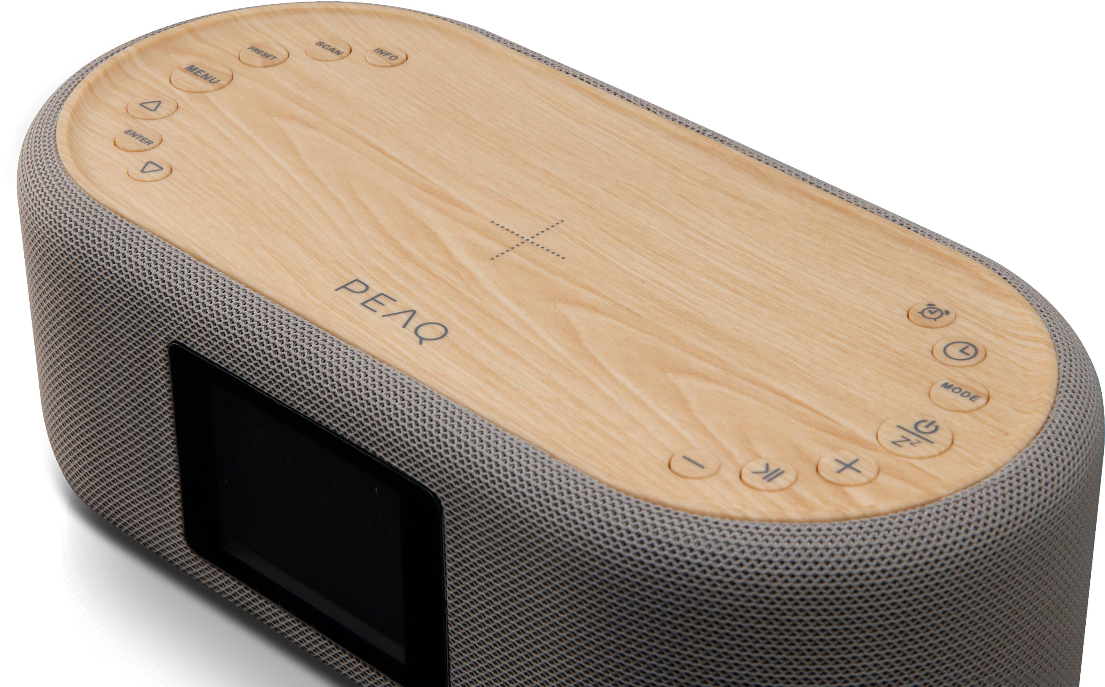 Ein grau- und holzfarbener Lautsprecher mit Knöpfen, einem kleinen Bildschirm und dem Wort 'PEAQ' oben.