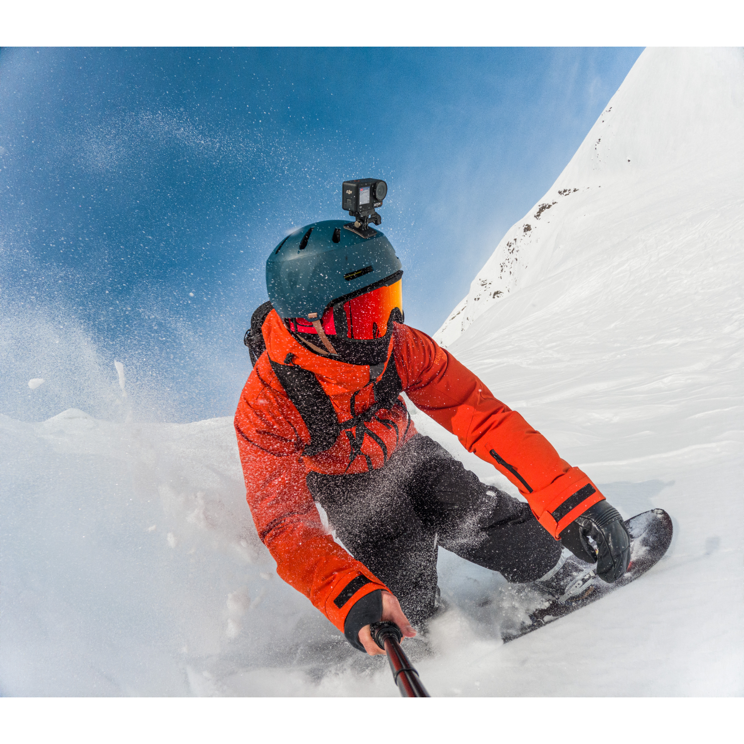 Snowboarder in de sneeuw, draagt oranje jas, helm met camera. Sneeuw en blauwe lucht.