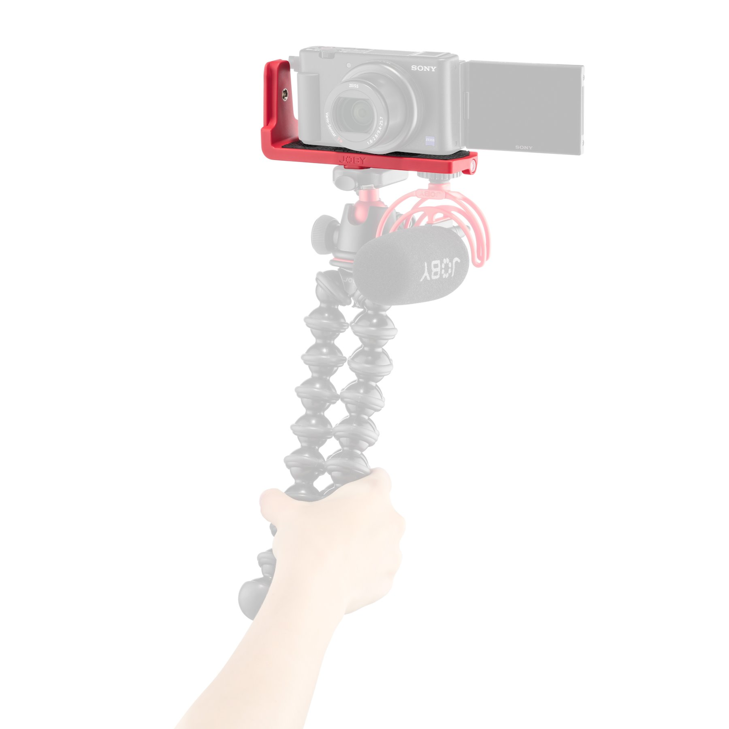 Fotocamera su supporto rosso, microfono e treppiede flessibile in mano, sfondo bianco.