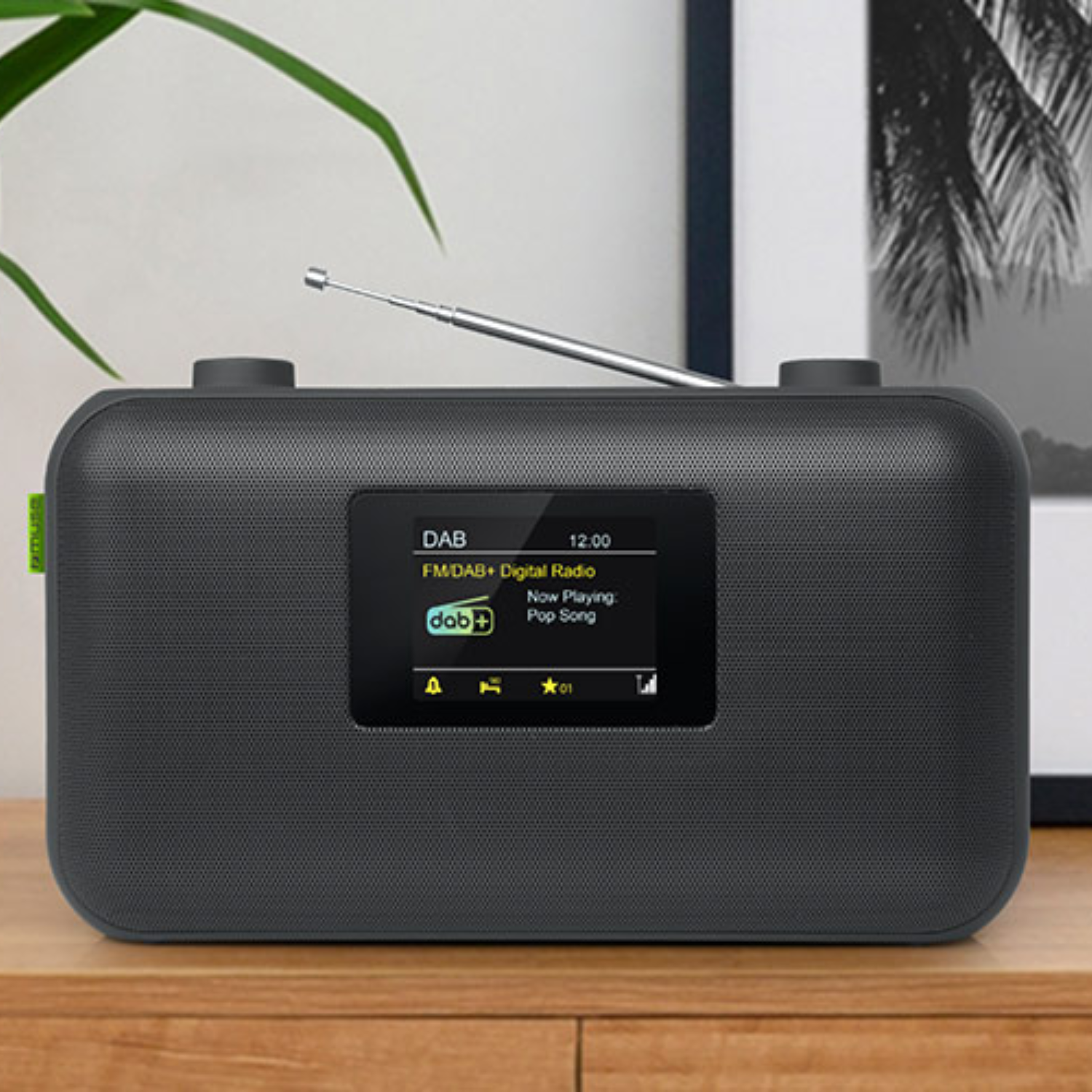 Dunkelgraues Radio mit Display, das Song-Infos zeigt, Antenne, auf Holzoberfläche, mit Bilderrahmen.