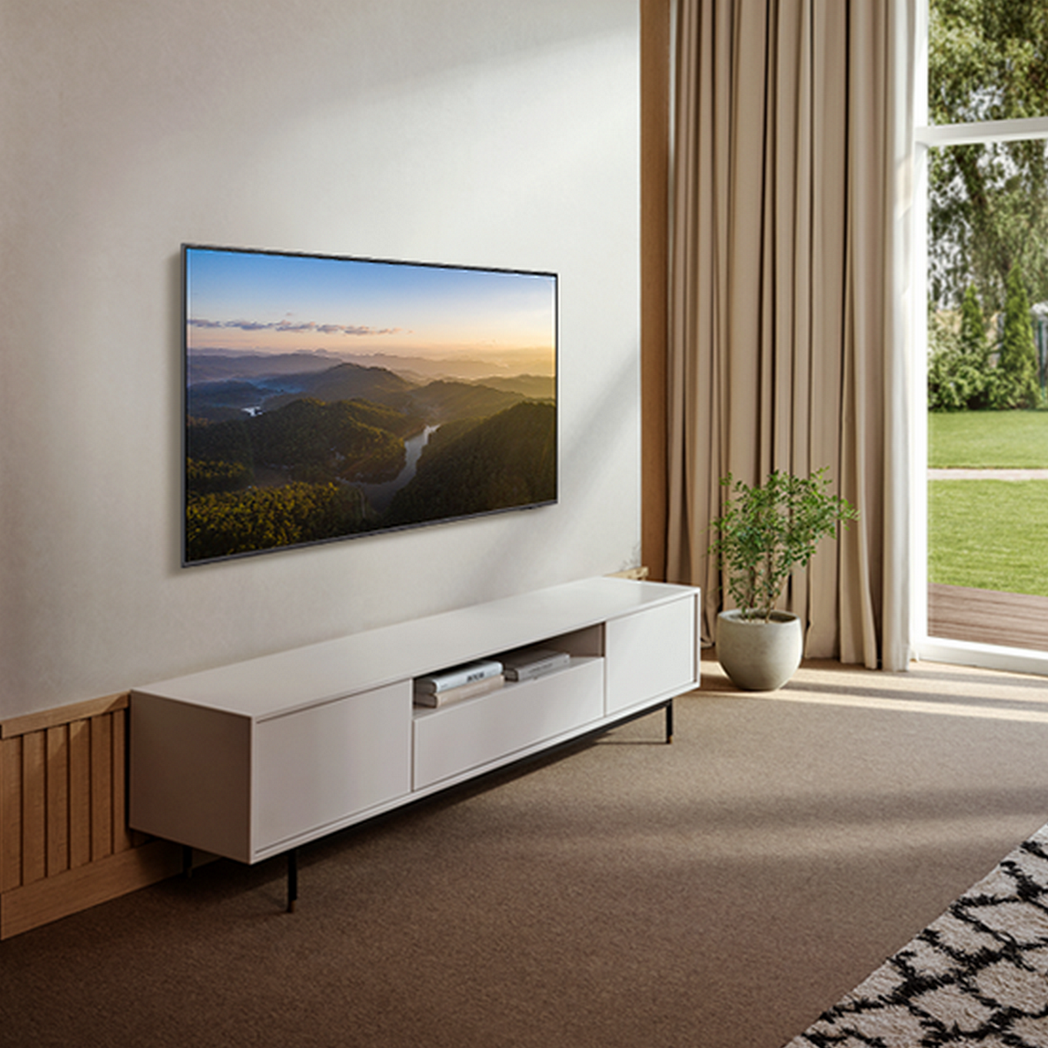 Telewizor zamontowany na ścianie nad białą szafką. Krajobraz wyświetlany na telewizorze. Zasłony i okno po prawej stronie.