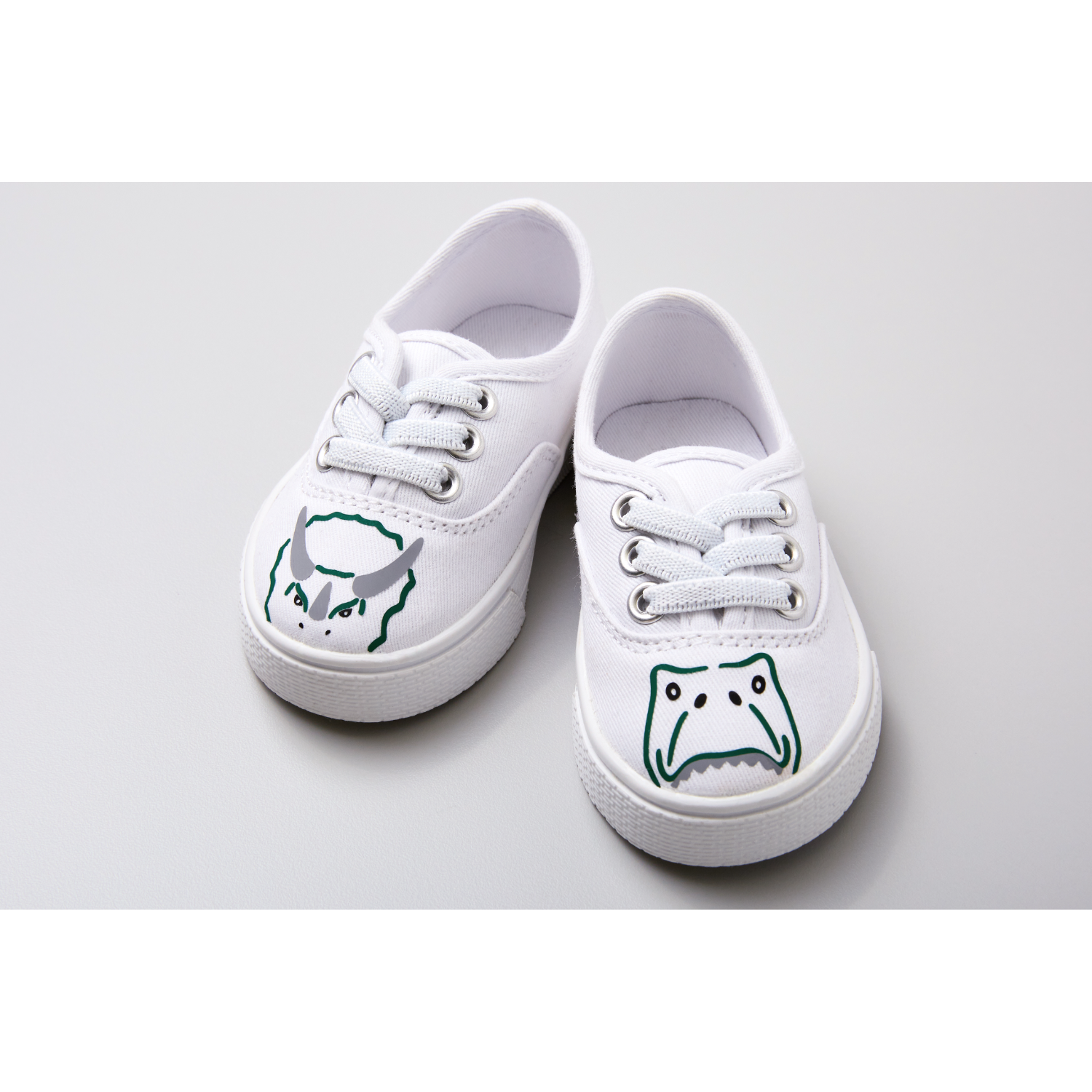 Zapatillas blancas con caras de monstruos de dibujos animados. Cada zapato tiene cordones y una cara de dibujos animados.