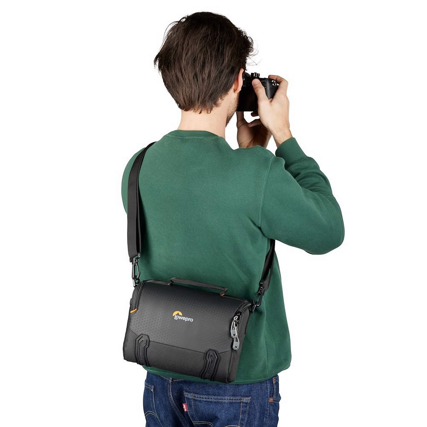 A person taking a photo with a camera, wearing a green sweater and a camera bag over their shoulder.