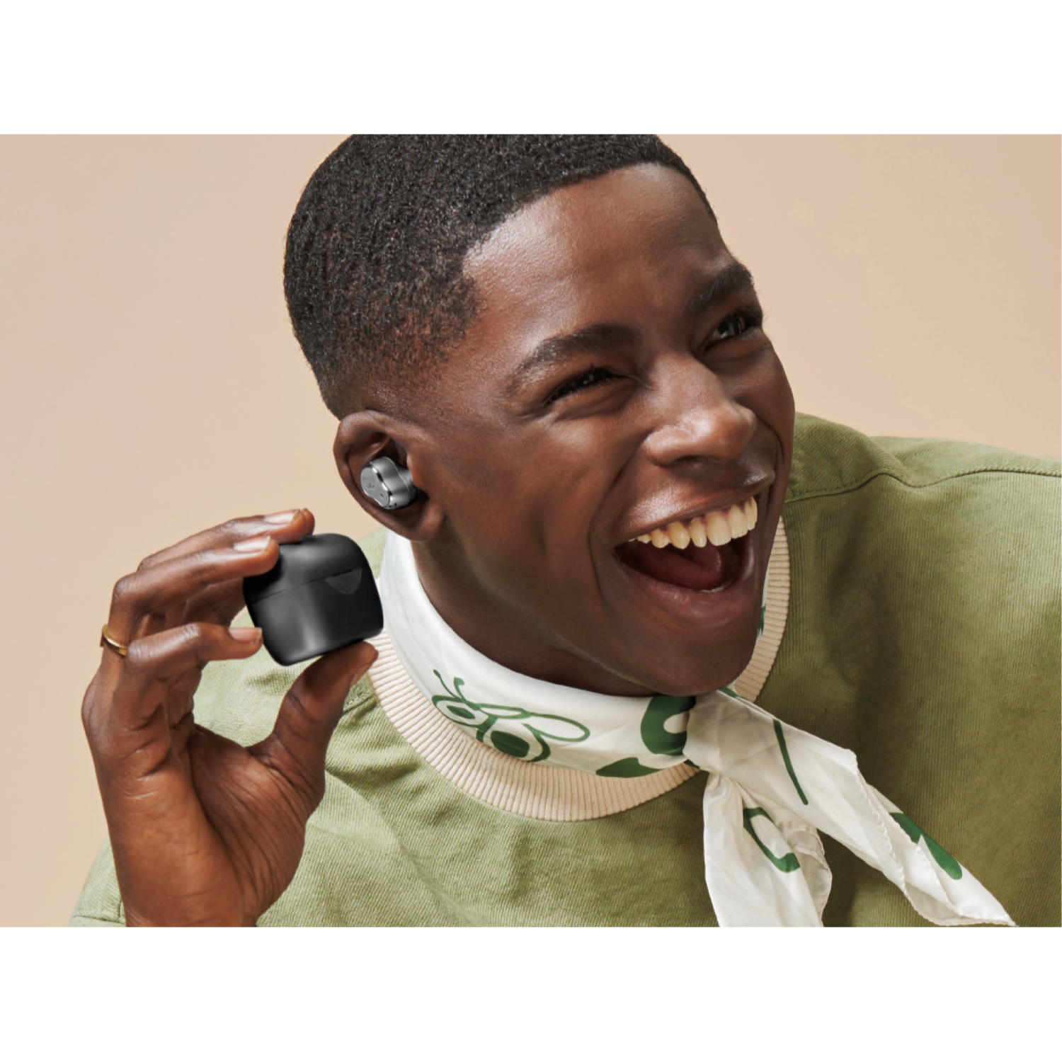 Happy man holding a black earbud case and wearing earbuds. Beige background.
