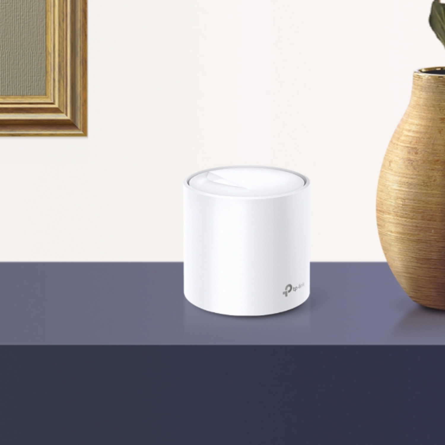 Ein weißer zylindrischer Router steht auf einem blauen Tisch. Ein goldgerahmtes Bild und eine Vase sind im Hintergrund.