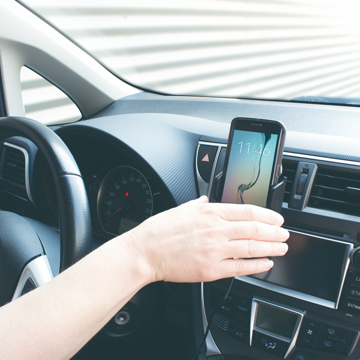 Hand die een telefoon in een auto vasthoudt. Telefoon toont 11:46, auto interieur.