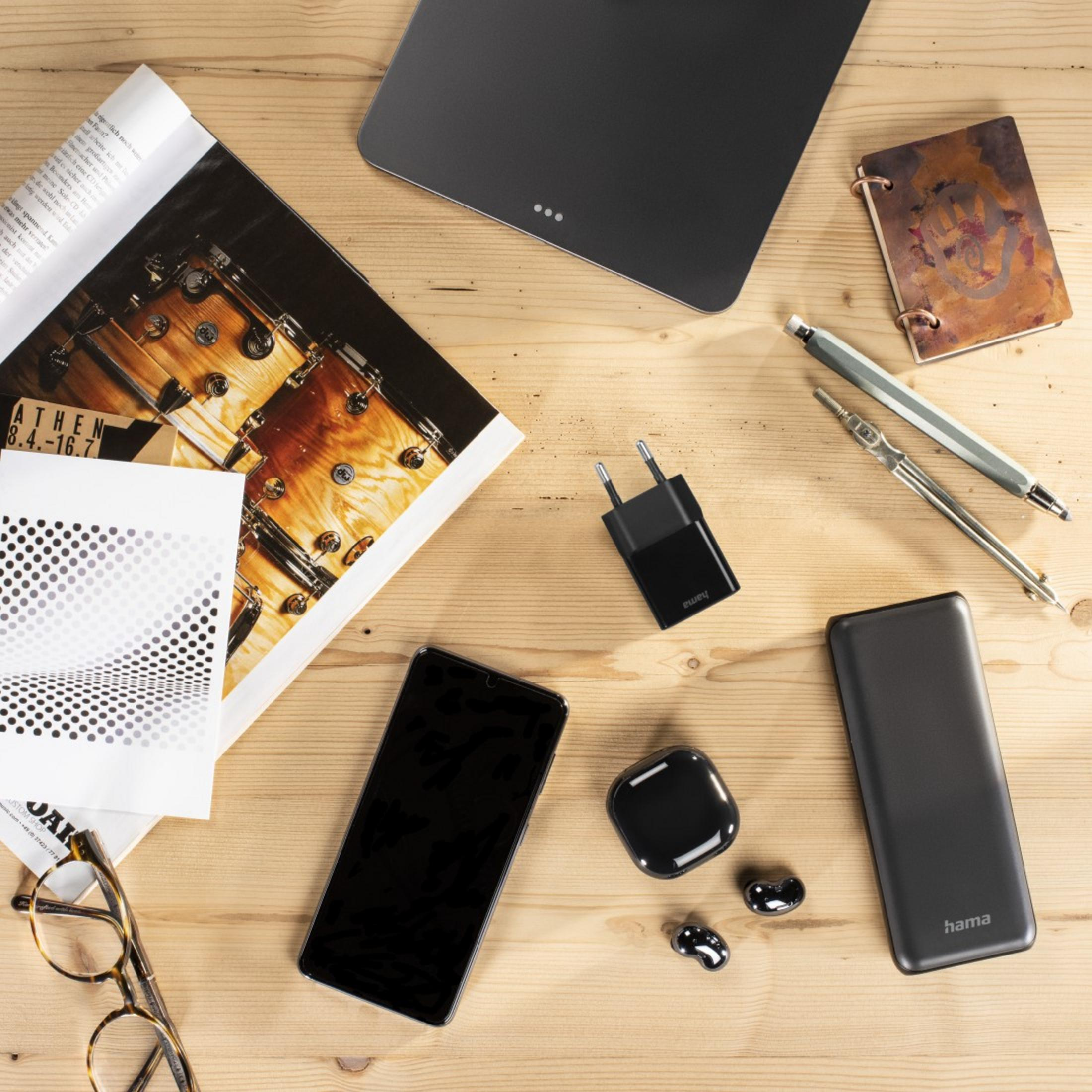 Biurko z telefonem, ładowarką, czasopismem, okularami, słuchawkami i innymi przedmiotami.