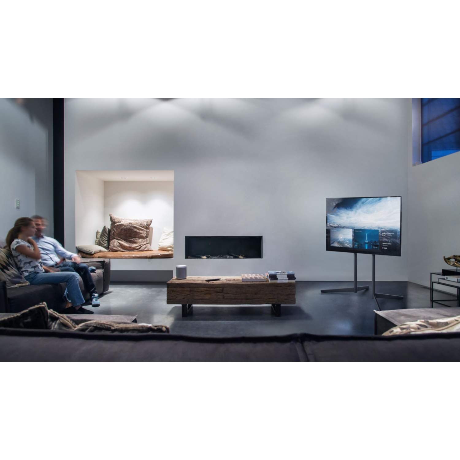 Wohnzimmer mit Personen. TV an der Wand, Tisch und Dekoration. Die Szene ist gut beleuchtet.