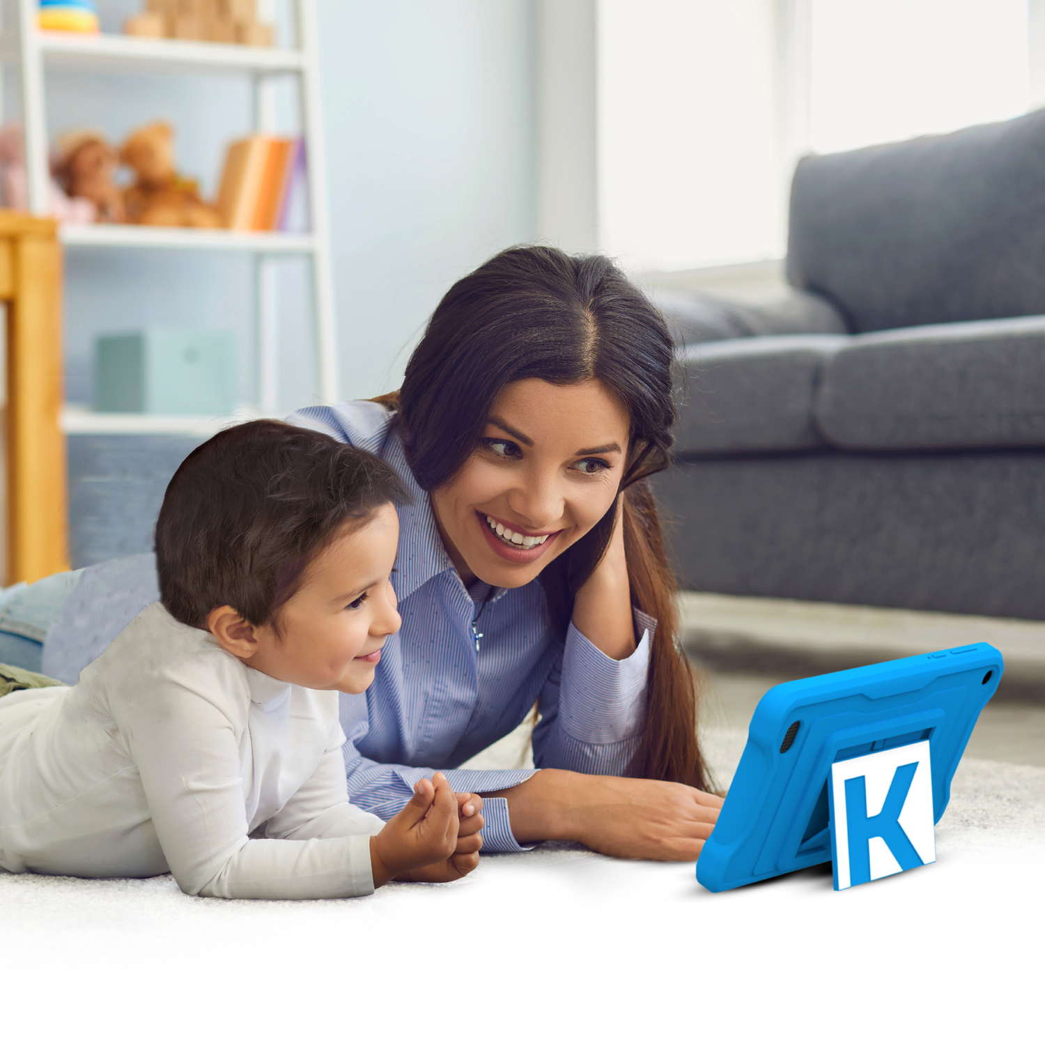 A woman and a child are on the floor looking at a blue tablet. The tablet has a white 'K' on it.